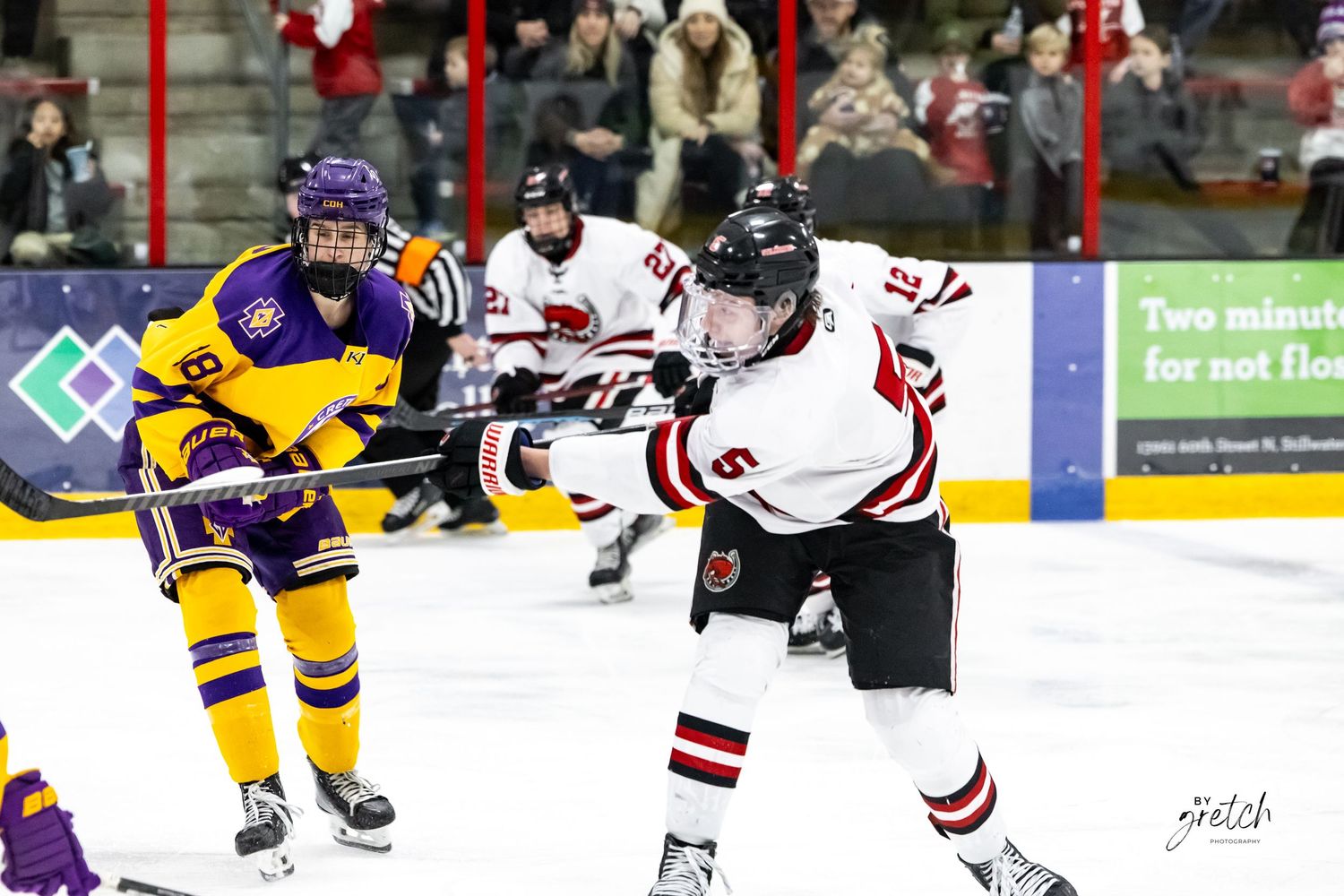 White jersey hockey player taking wrist shot during competitive ice hockey game.