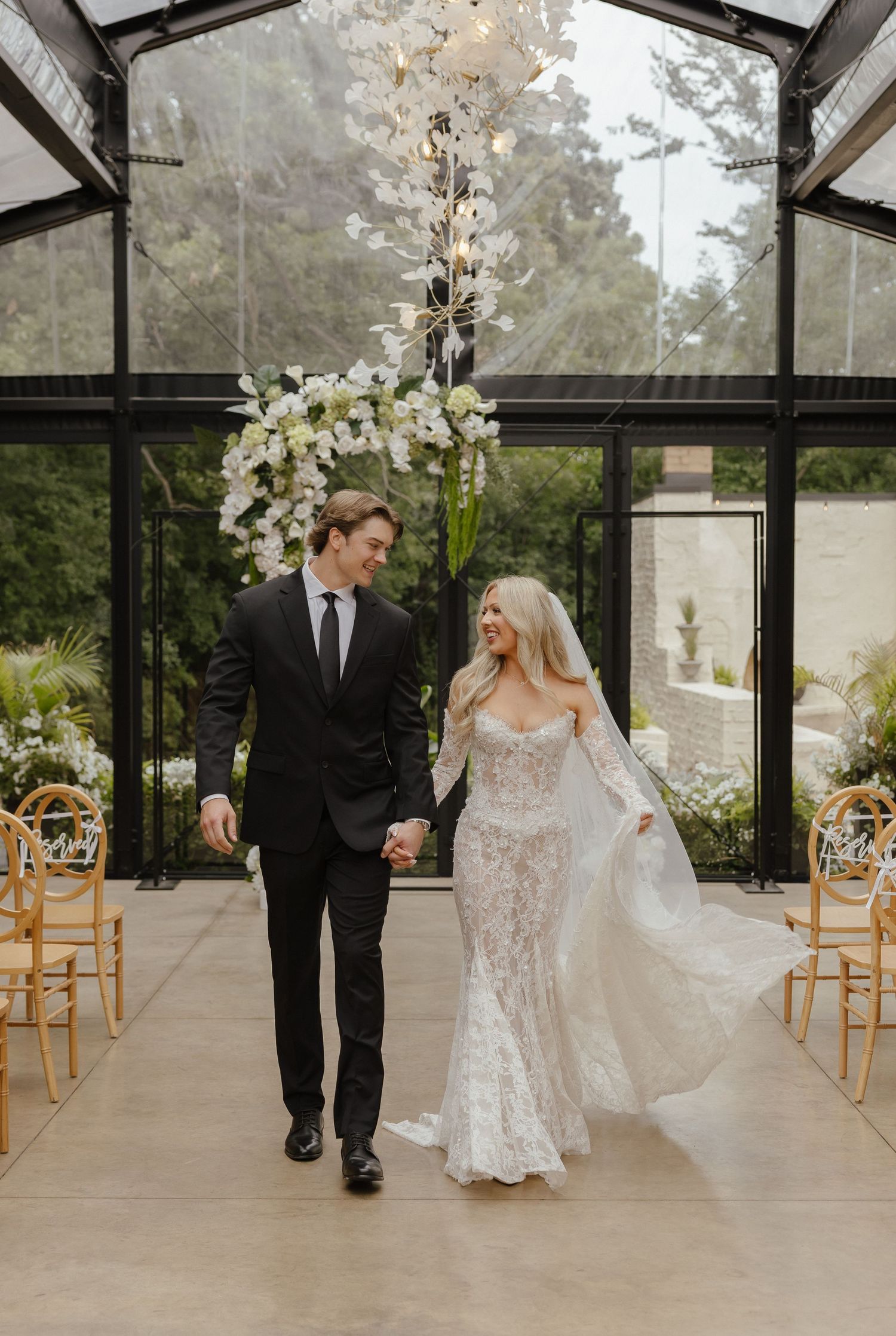 Bride and groom walking hand in hand down the aisle of a stunning glass greenhouse wedding venue.