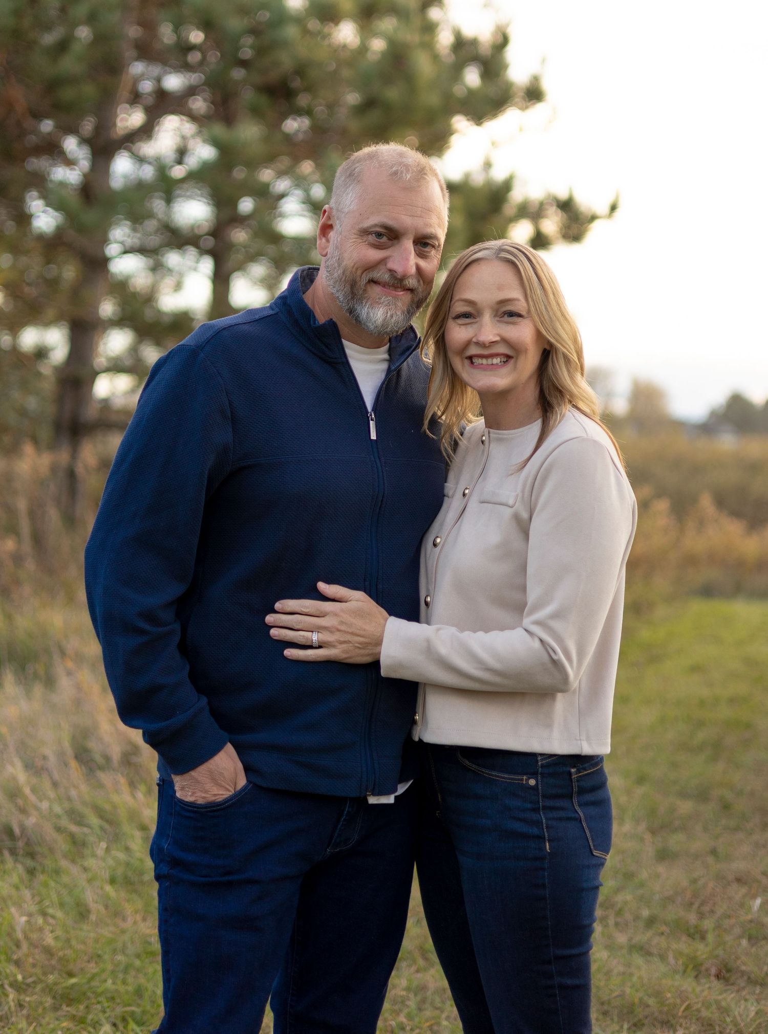 Happy middle-aged couple posing together in a scenic outdoor field during fall season.