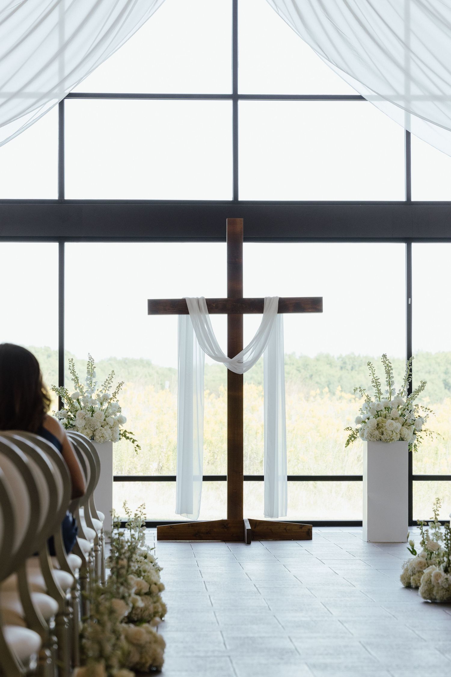 Elegant wedding chapel altar with wooden cross, white draping, and floral arrangements.