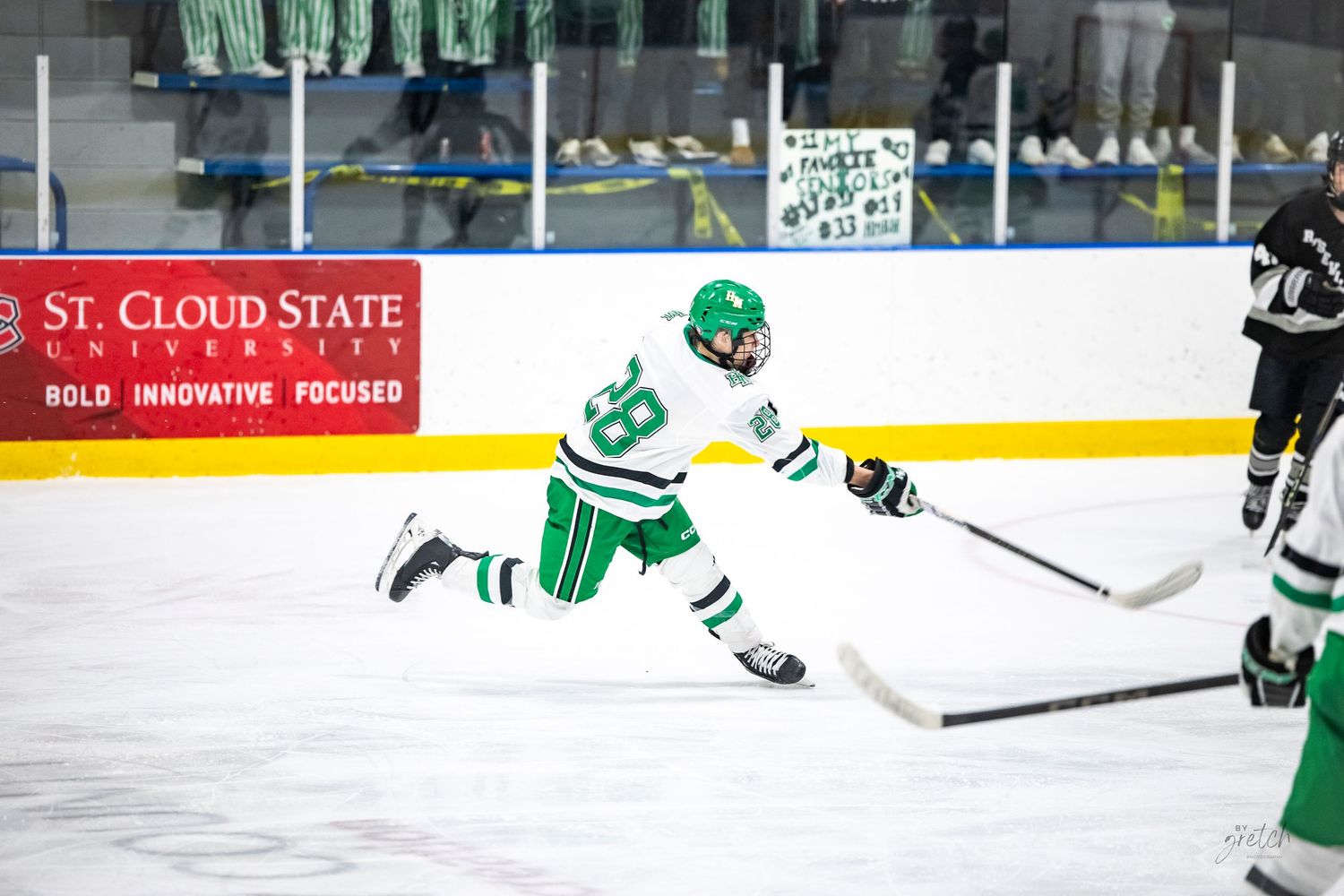 Hill-Murray Pioneers player taking a shot on ice near St. Cloud State University arena boards.