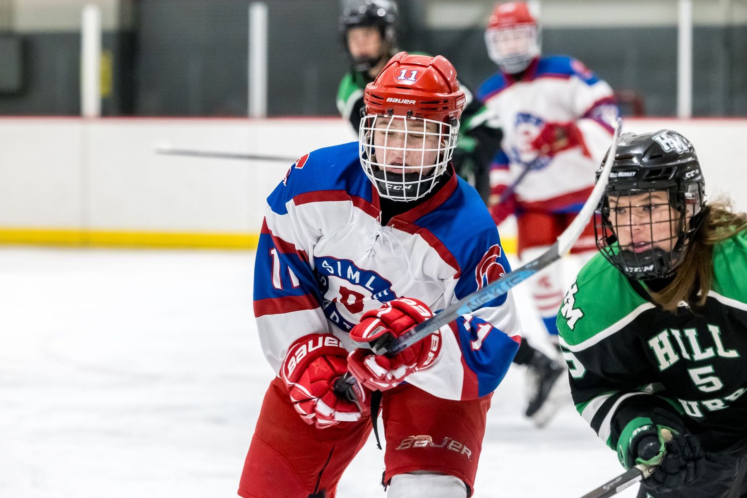 Two youth hockey players in red-white-blue and green uniforms competing on ice.