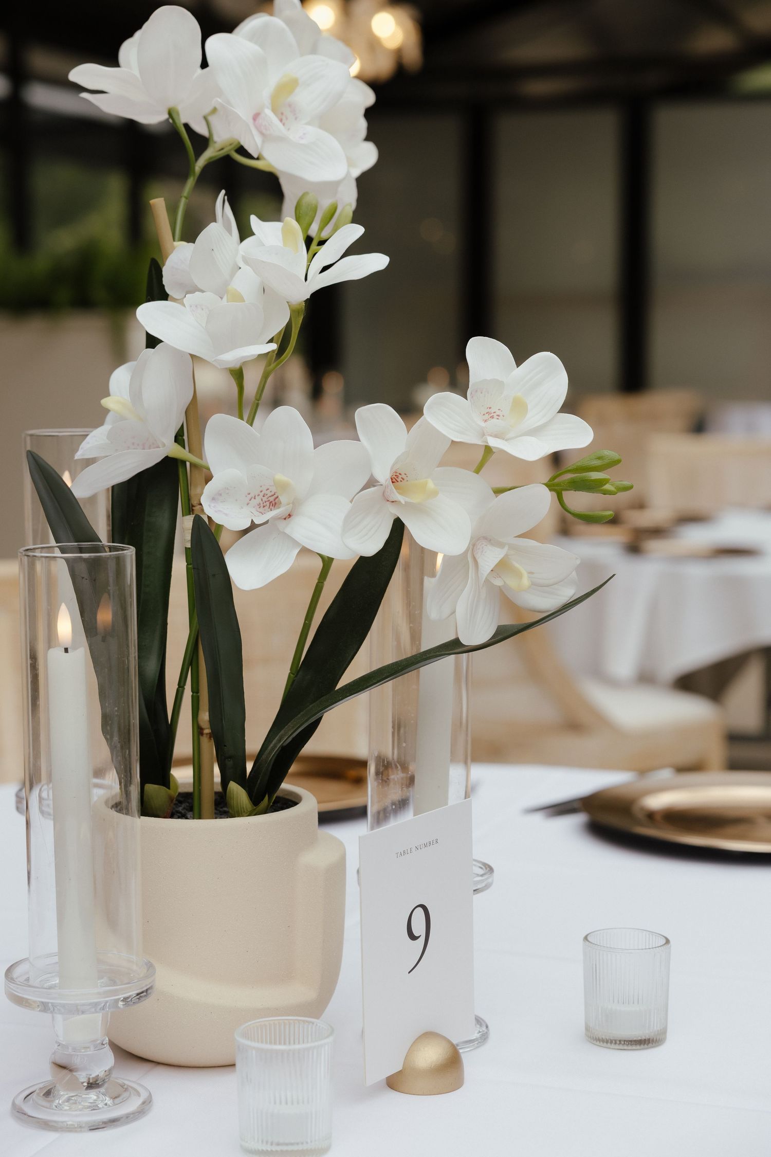 Elegant white orchid centerpiece with gold accents and table number nine at a wedding reception.