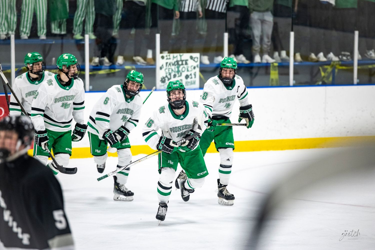 Youth hockey team in green uniforms skating on ice during a competitive game.