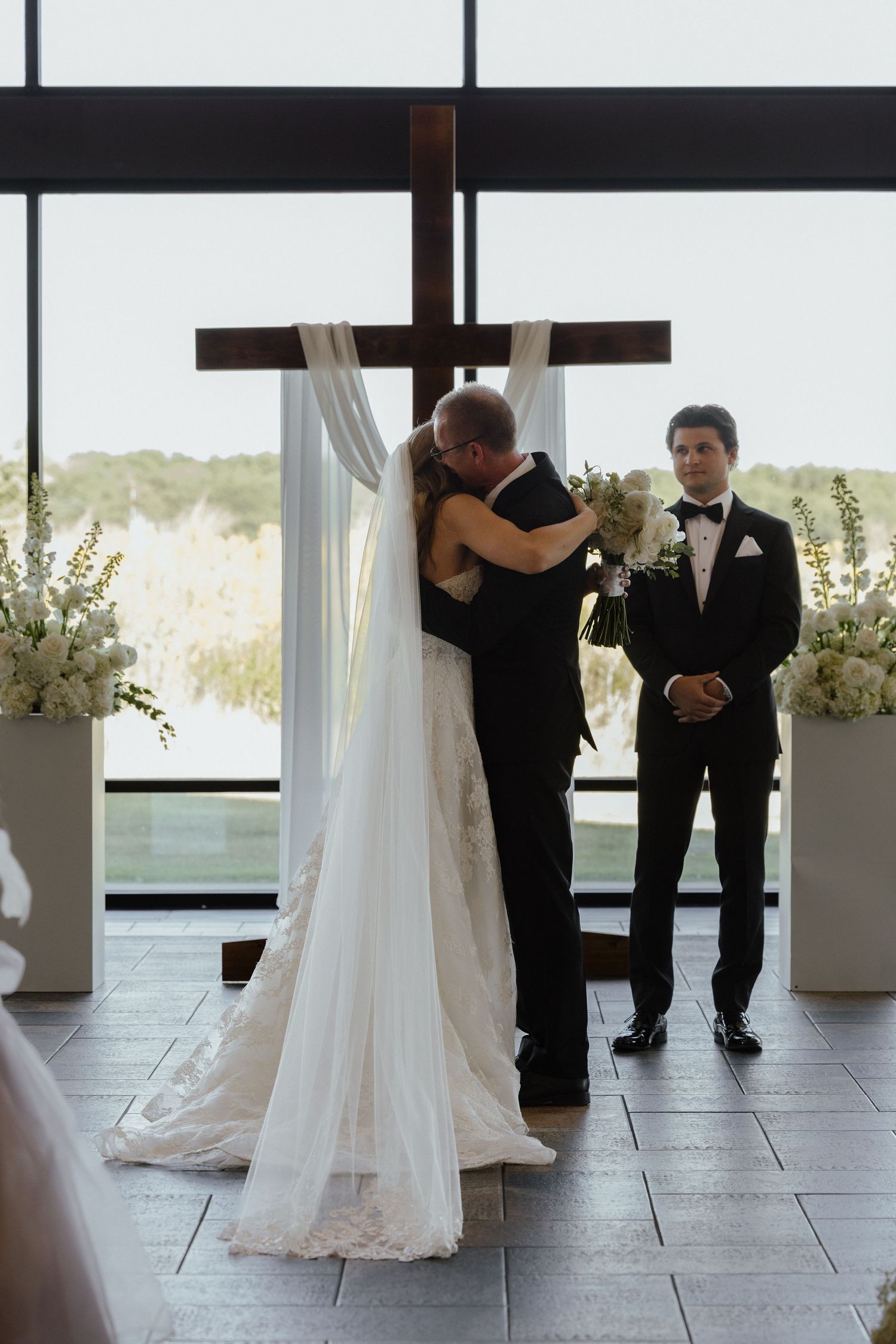 Bride and groom share first kiss at altar with wooden cross backdrop.