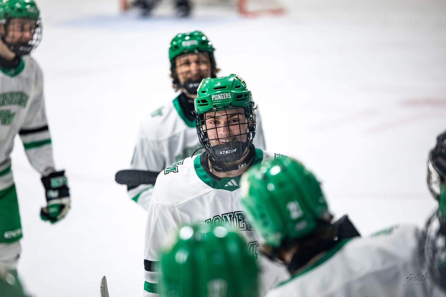 Youth hockey players in green uniforms huddle on ice rink during a game.