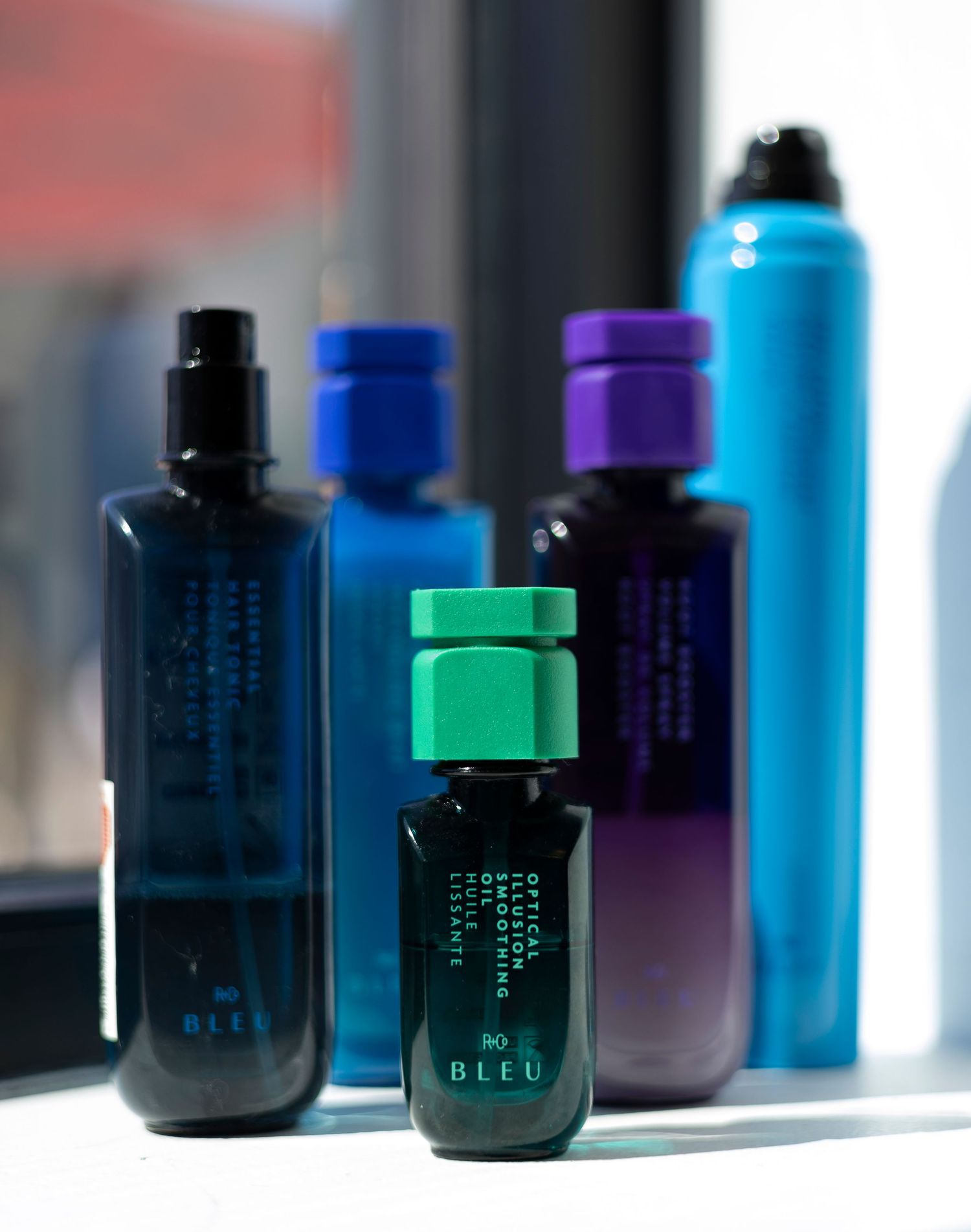 Collection of R+Co Bleu luxury hair care products displayed on a windowsill in a salon.