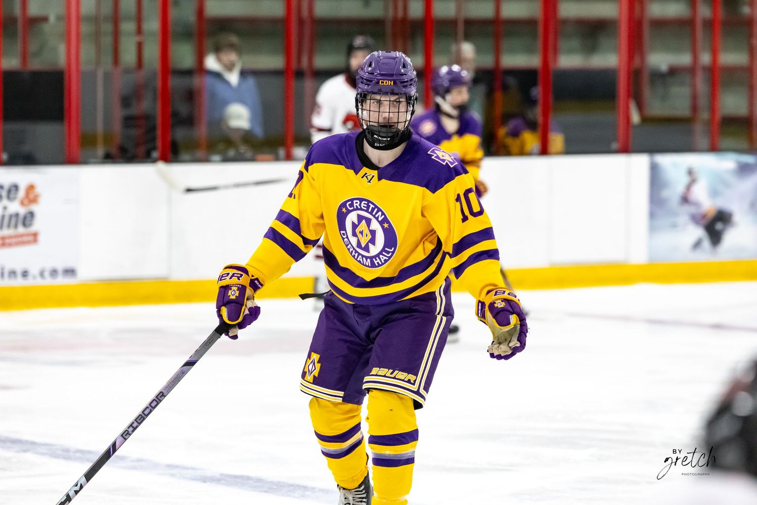 Youth hockey player in purple and gold uniform skating on ice during game.