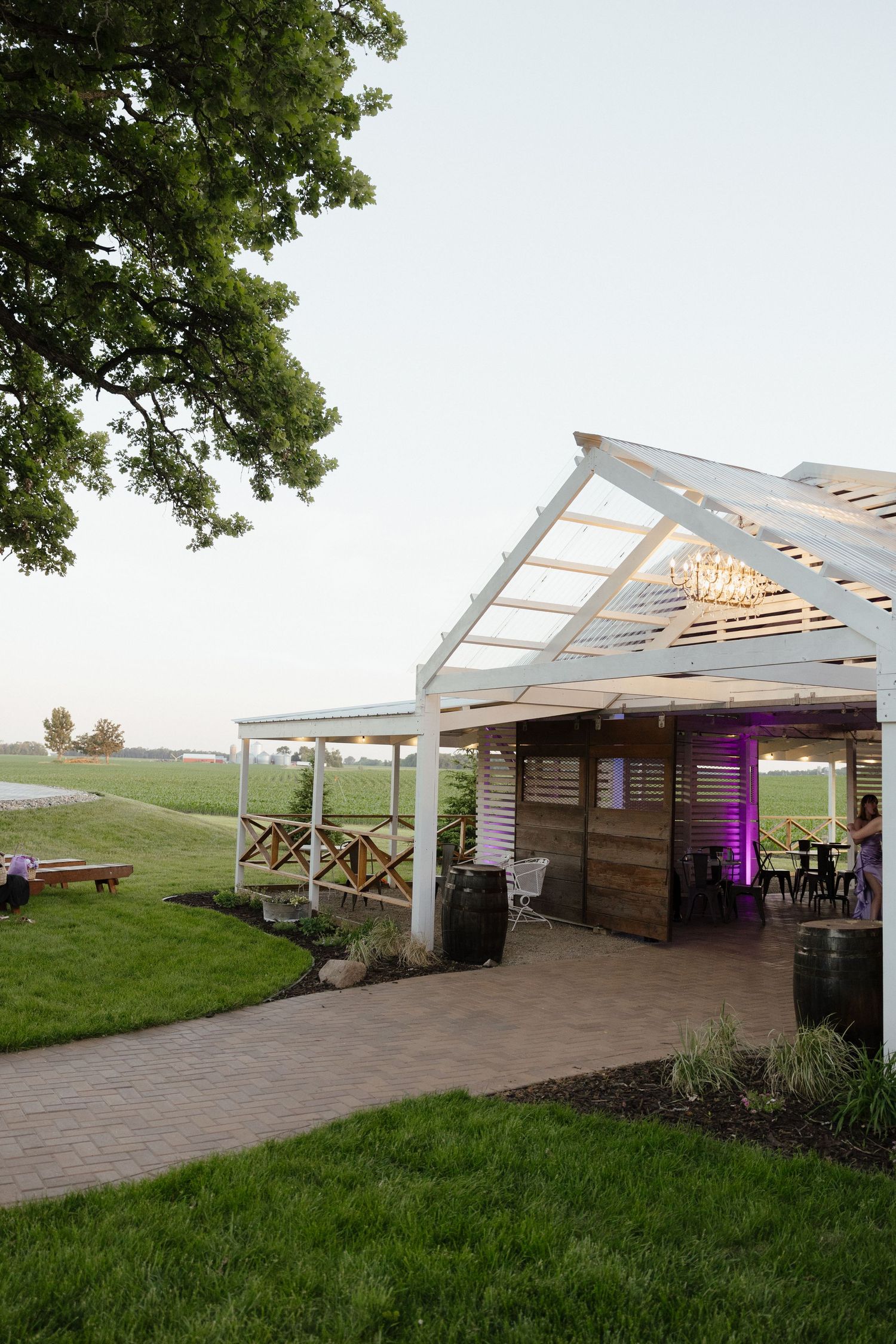 Rustic white open-air pavilion with string lights and wood accents at a farm wedding venue at dusk.