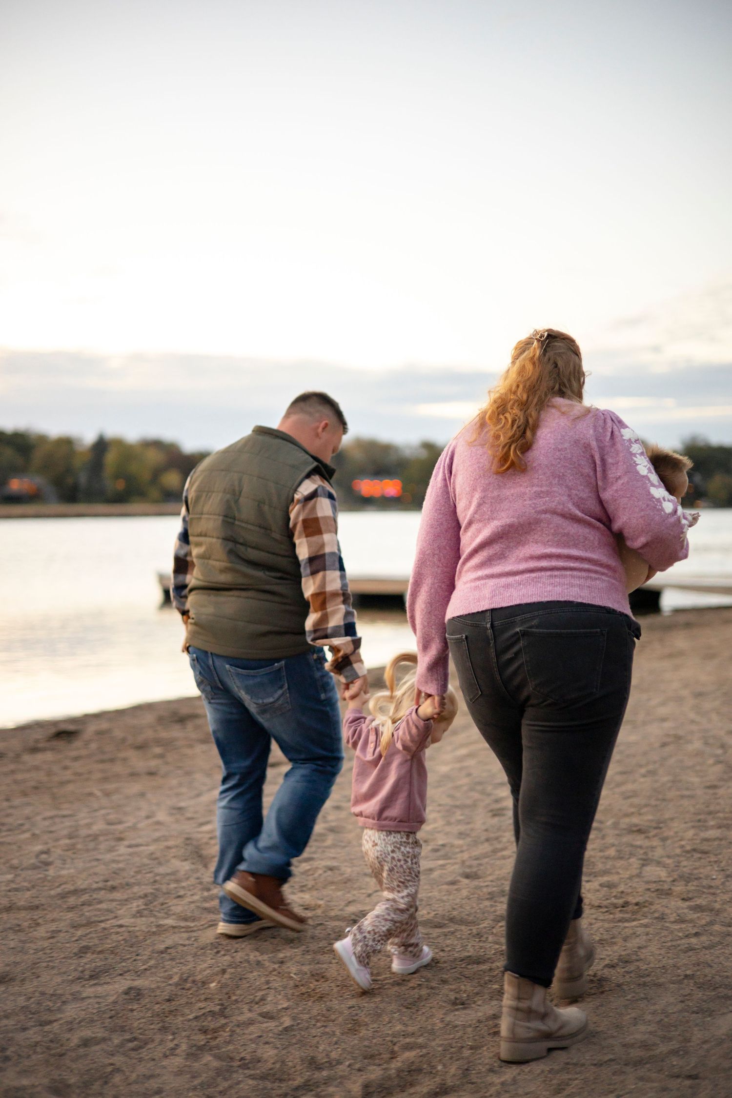 Family of four walking hand in hand along sandy beach at sunset.