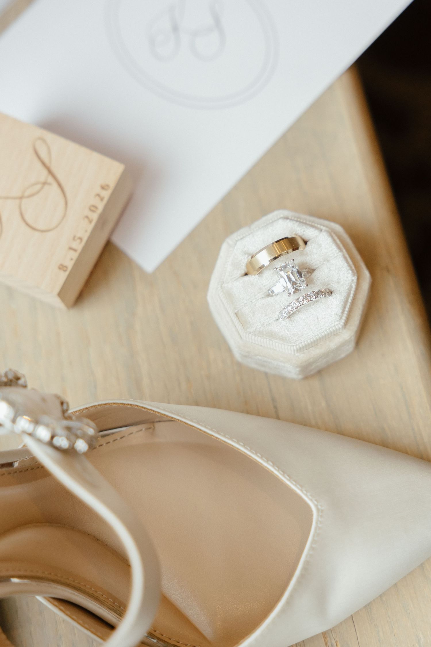Wedding flat lay featuring diamond engagement ring, gold band, pearl heels, monogram stamp, and stationery.