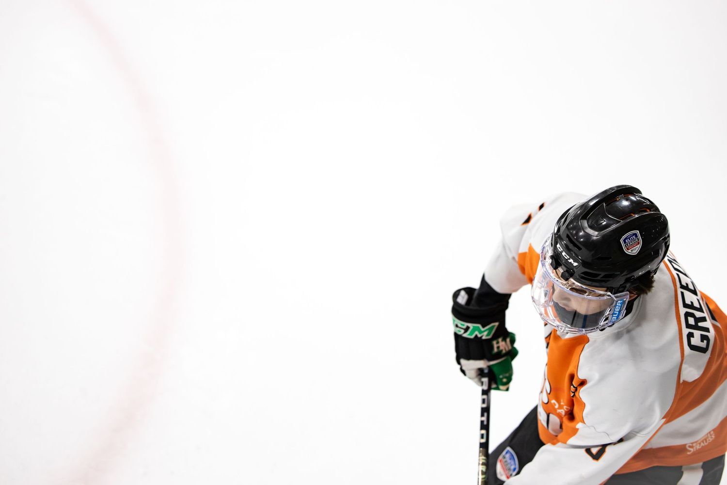 Overhead view of hockey player in orange and white uniform holding stick on ice.
