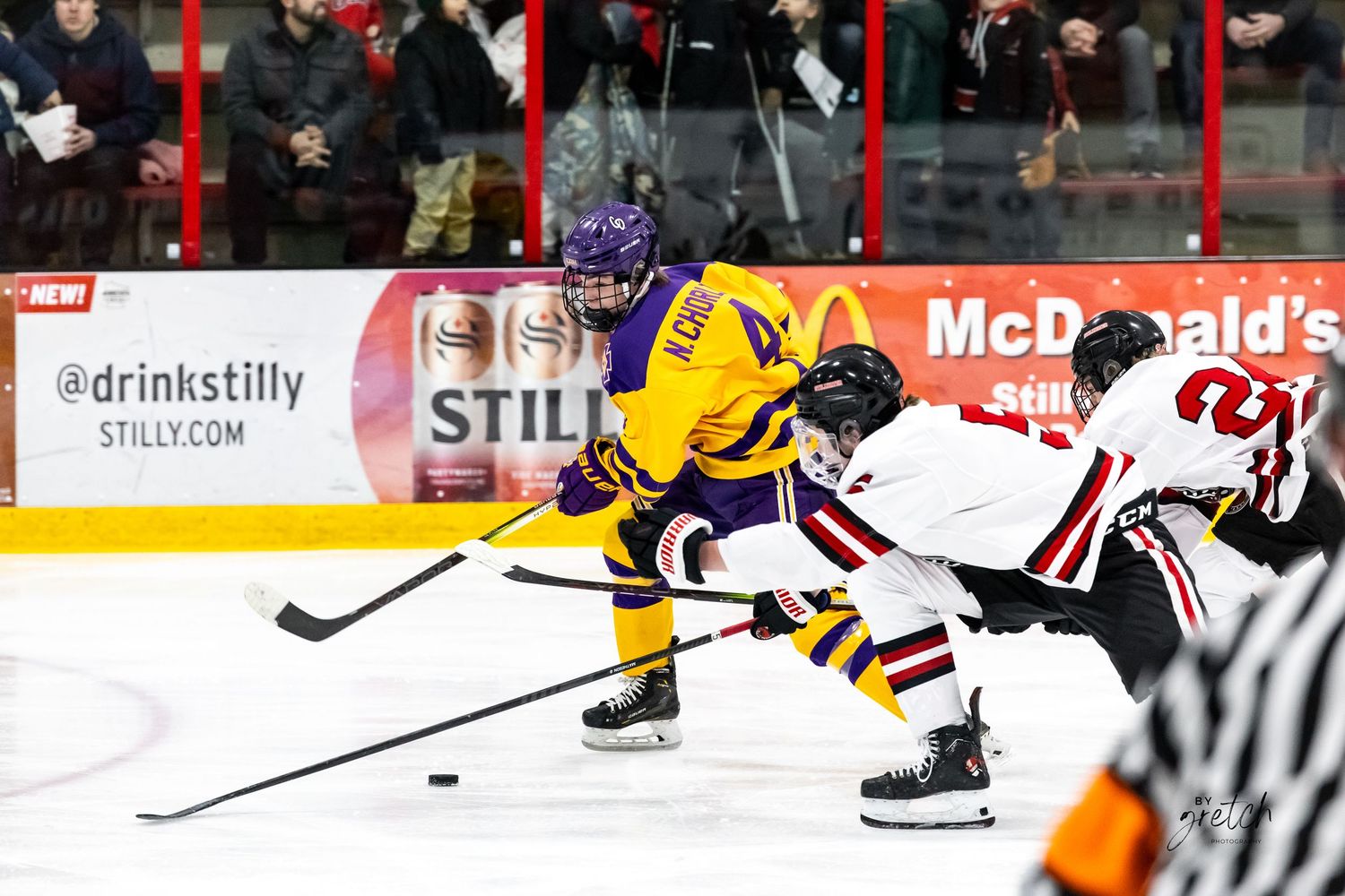 Two hockey players competing for puck along boards during youth hockey game.