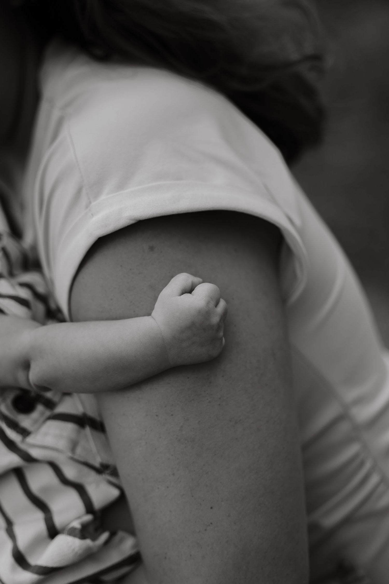 Black and white photo of a baby's tiny fist grasping a mother's arm, symbolizing love and connection.