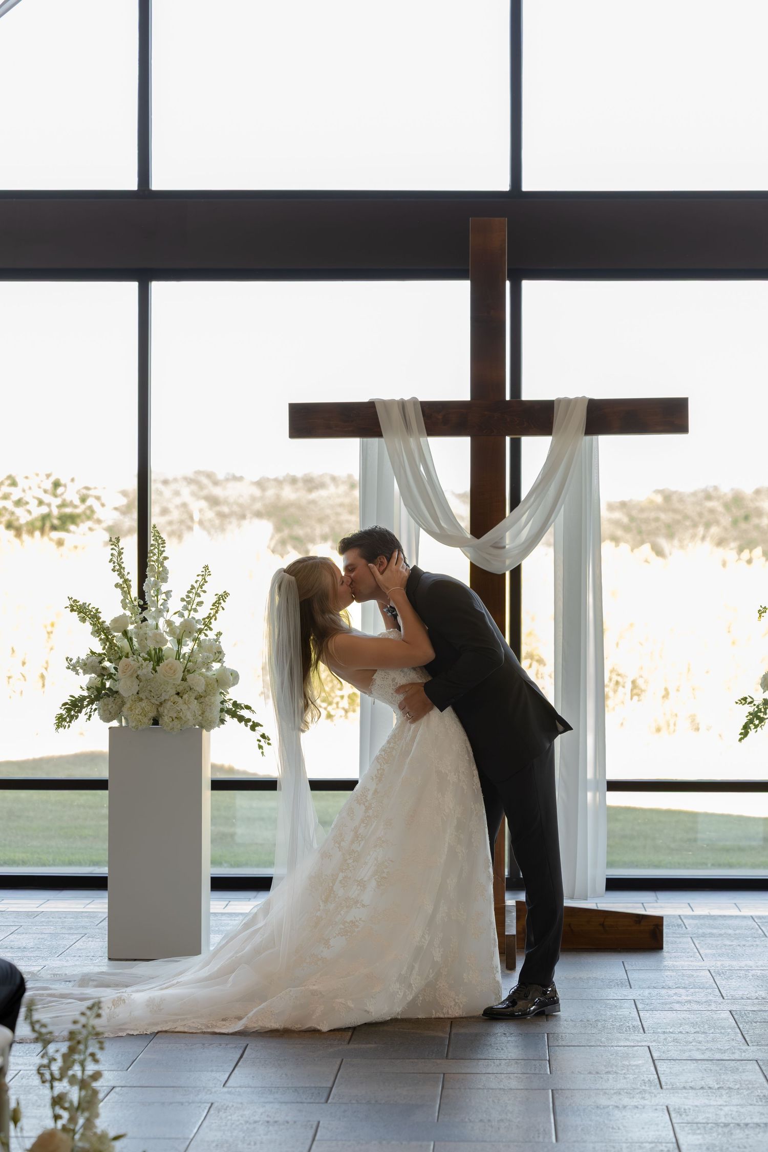 Bride and groom share romantic first kiss at chapel altar with cross.