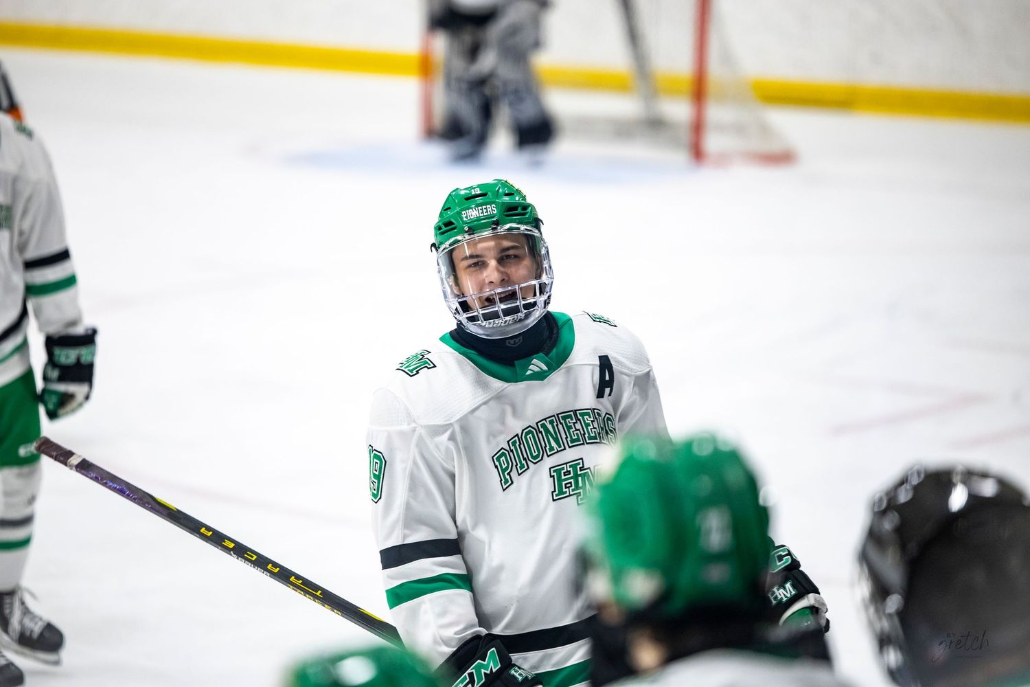 Youth hockey player in green Pioneers jersey smiling on the ice rink.
