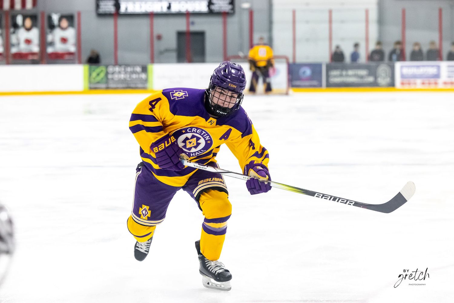 Youth hockey player in purple and gold uniform taking a shot on ice.