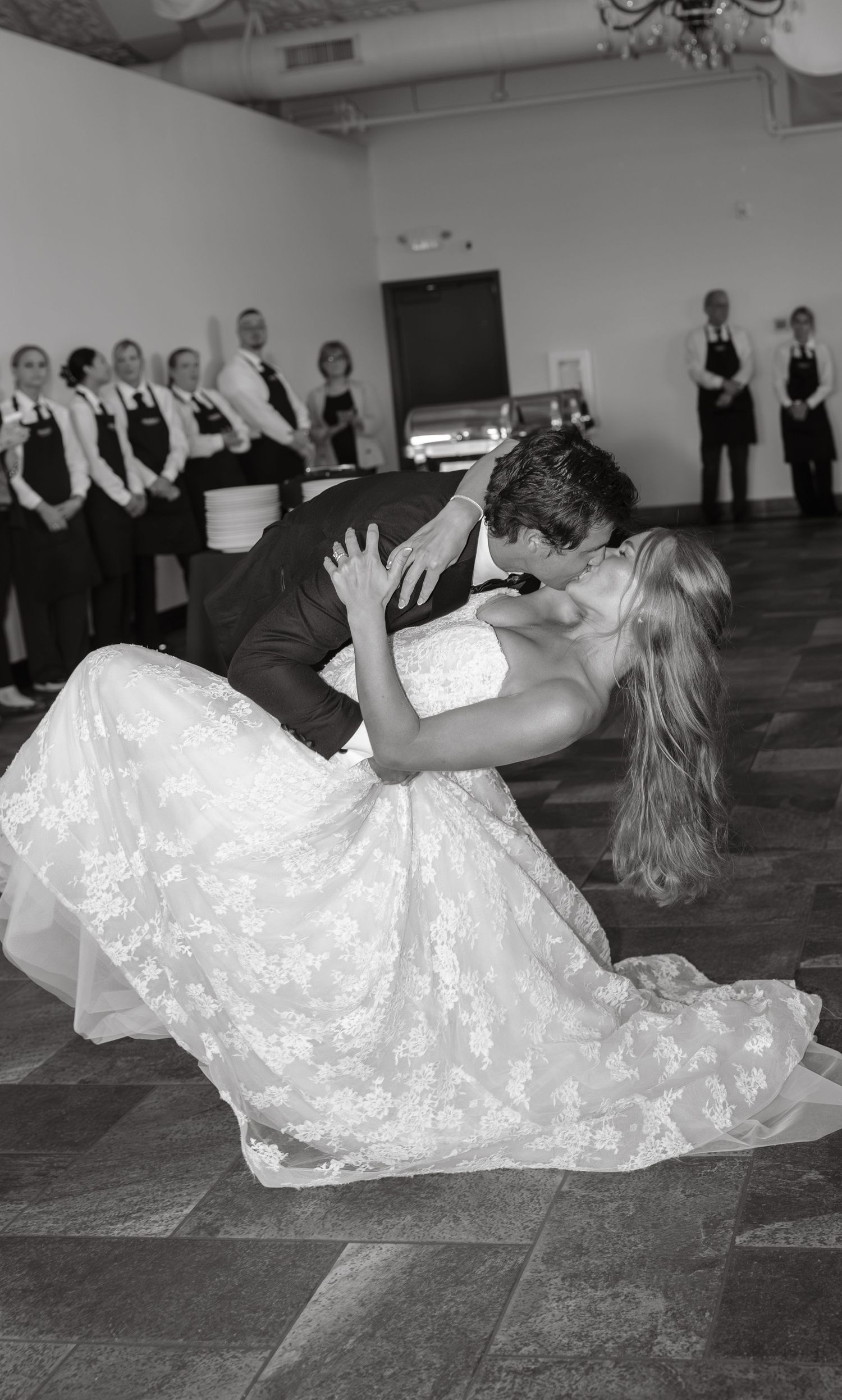 Black and white photo of groom dipping bride in a romantic first dance kiss at their wedding reception.