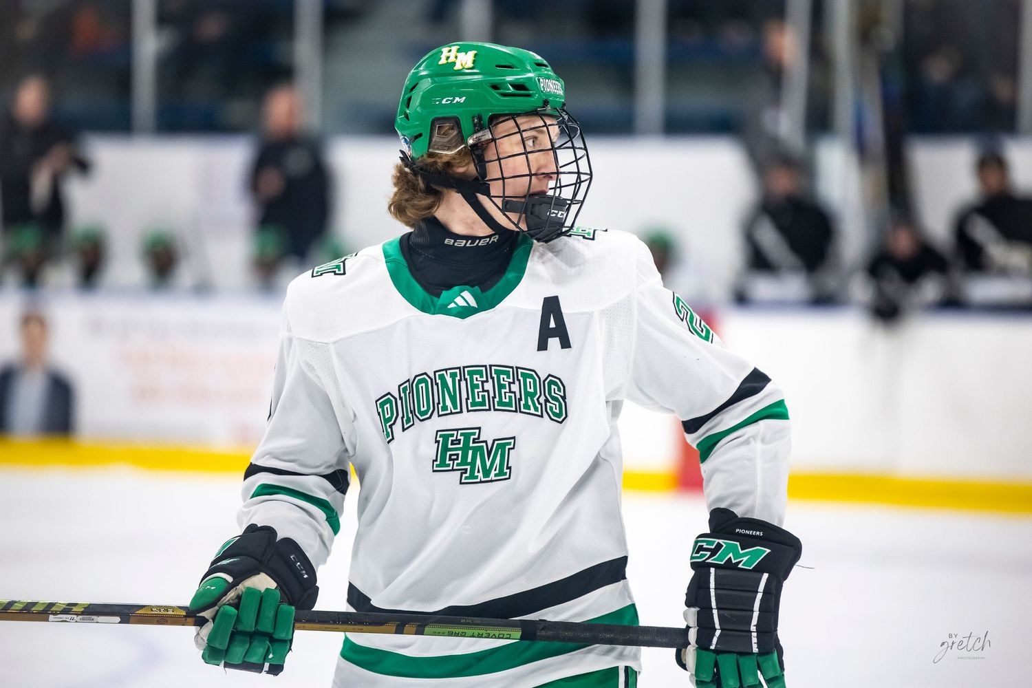 Hill-Murray Pioneers hockey player wearing green and white jersey with letter A on the ice.
