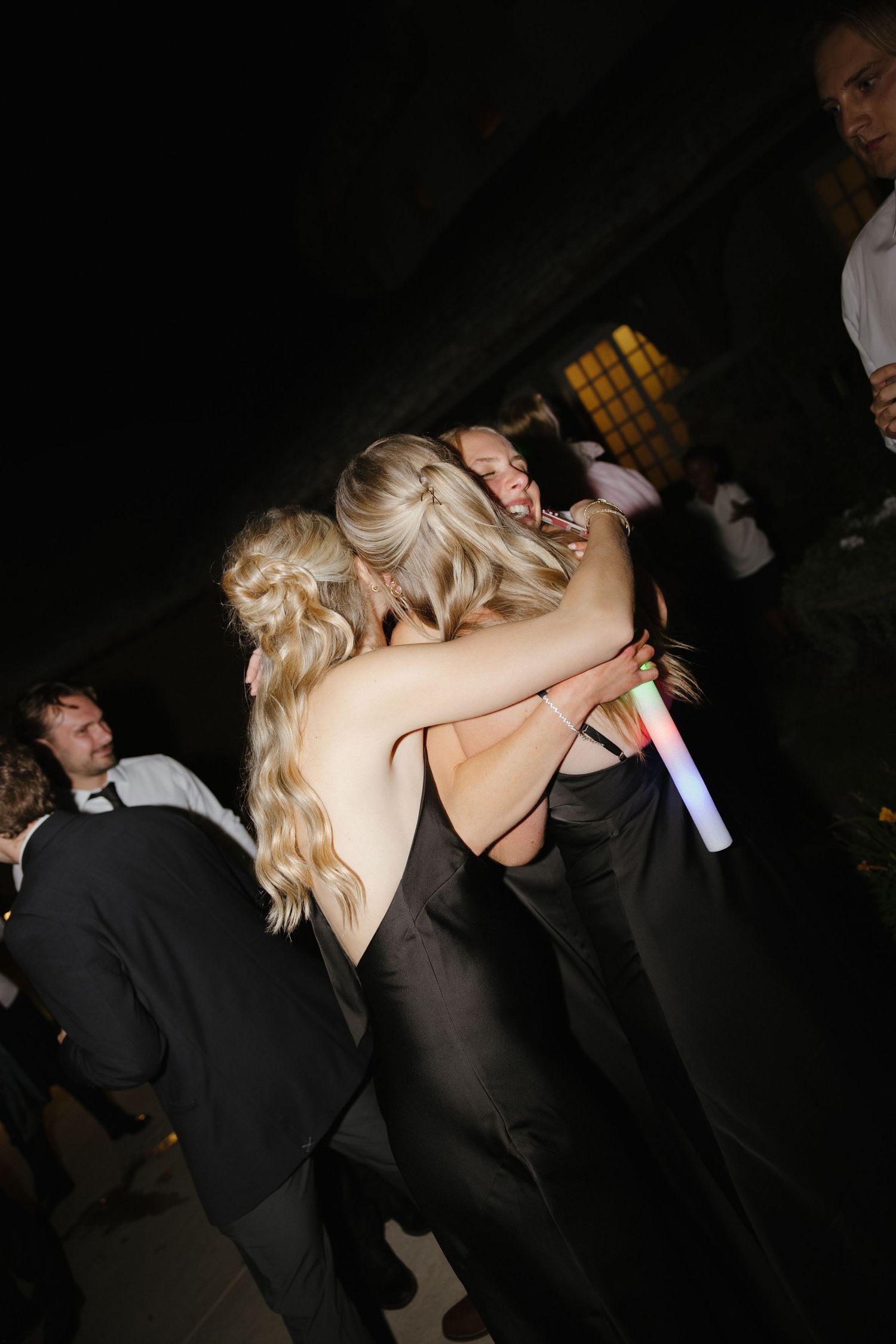 Two women in black dresses hugging and dancing at a dark wedding reception party.
