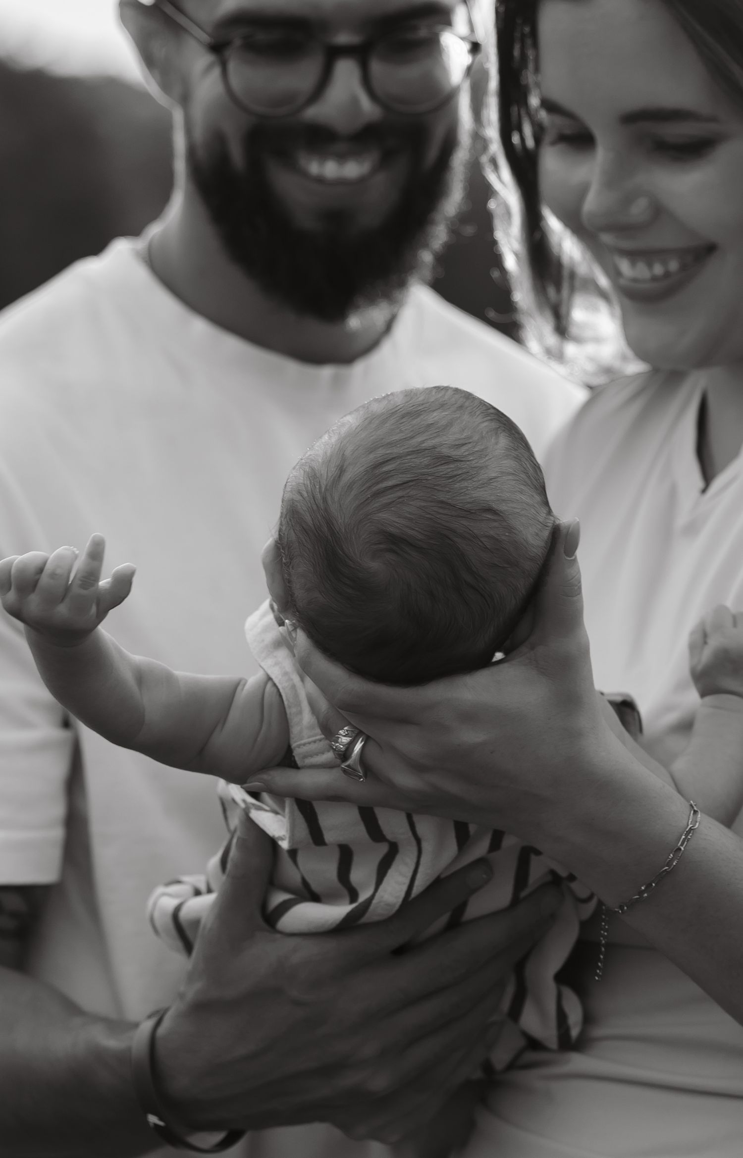 Black and white photo of happy parents smiling while holding their newborn baby, father with beard and glasses.