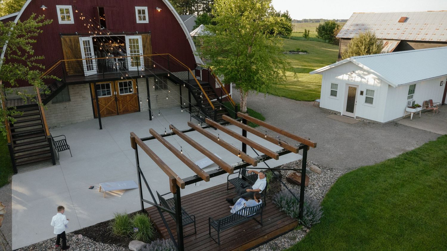 Aerial view of a red barn wedding venue with pergola, patio, and white greenhouse on a rural property.