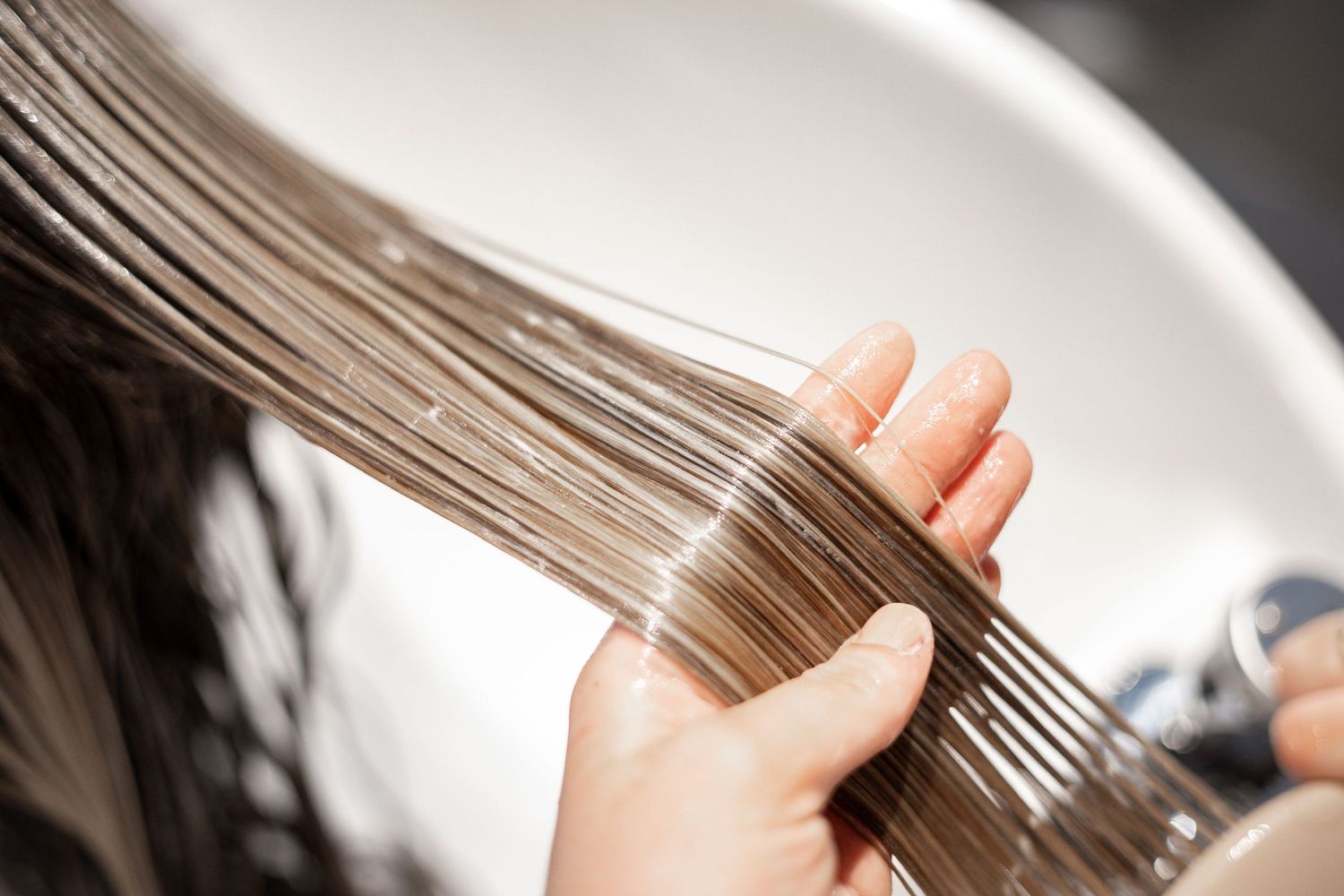 Close-up of a hairstylist combing through wet highlighted hair at a salon wash basin.
