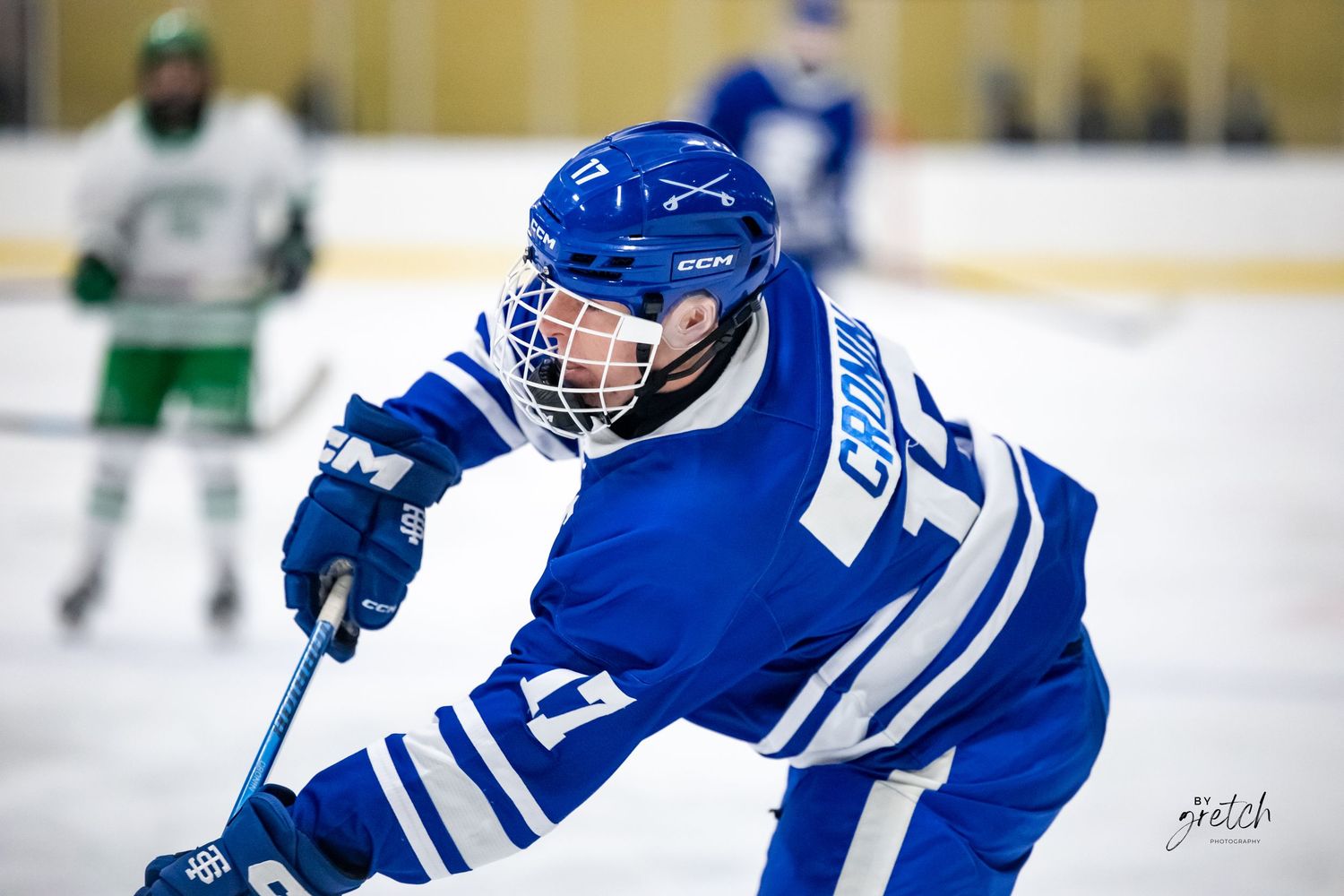 Youth hockey player in blue uniform skating with stick on ice rink.