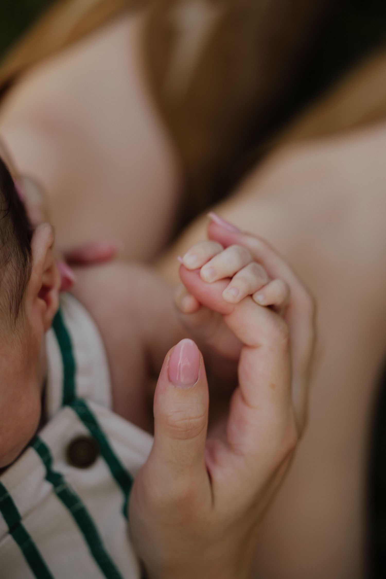 Close-up of newborn baby's tiny hand gripping mother's finger with pink manicured nail.