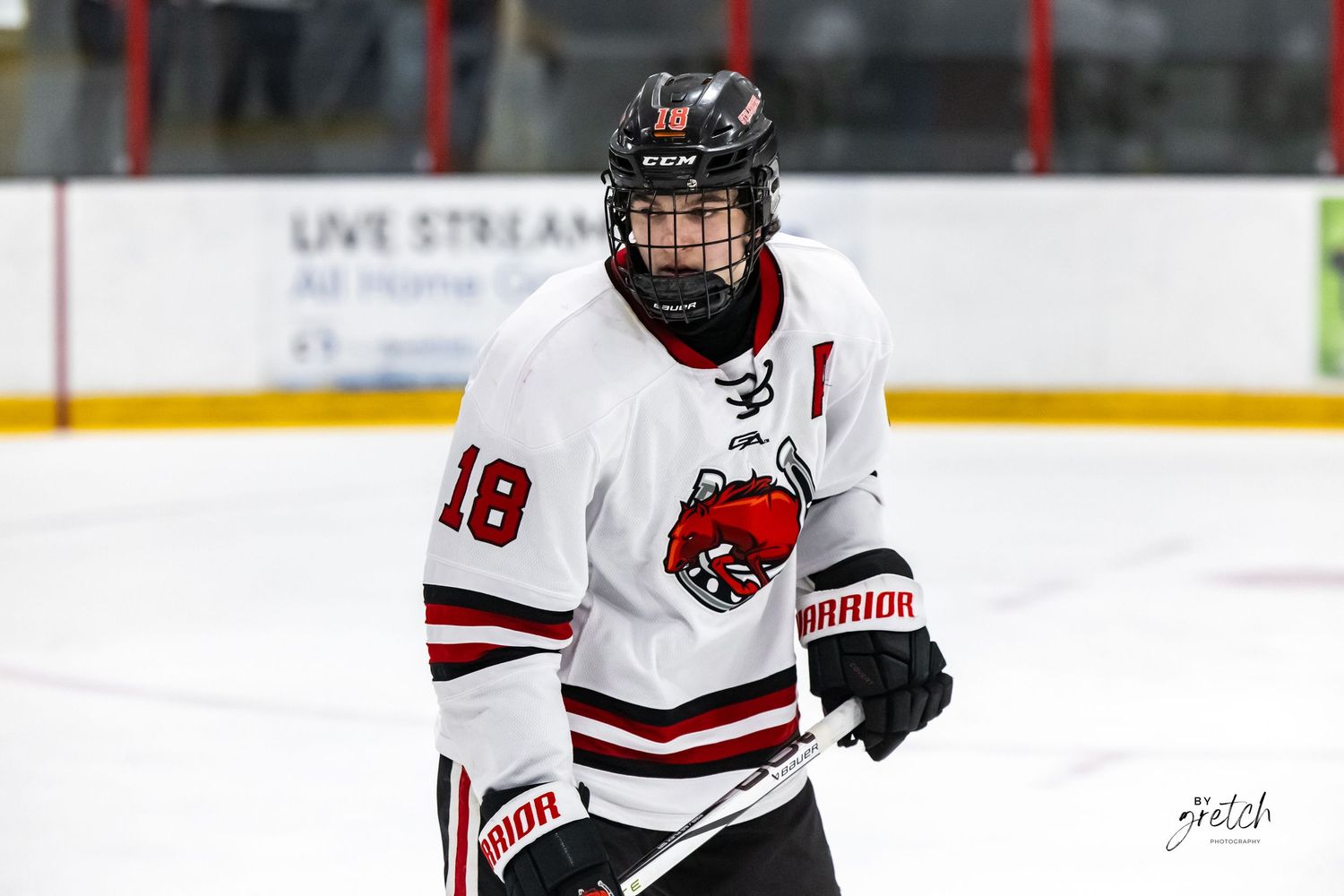Youth hockey player wearing white number 18 jersey skating on indoor ice rink.