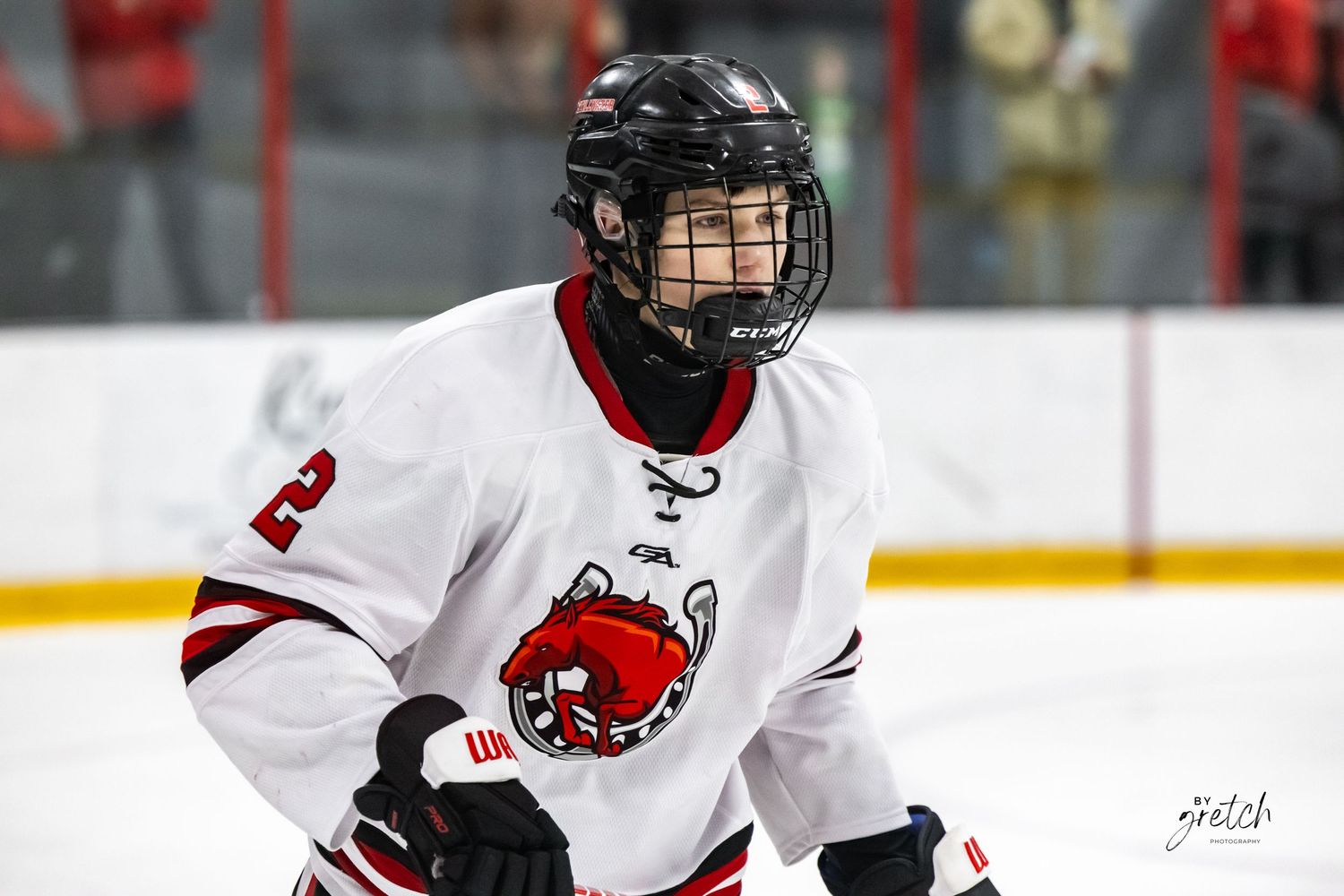 Hockey player wearing number 2 white and red jersey skating on ice rink during a game.