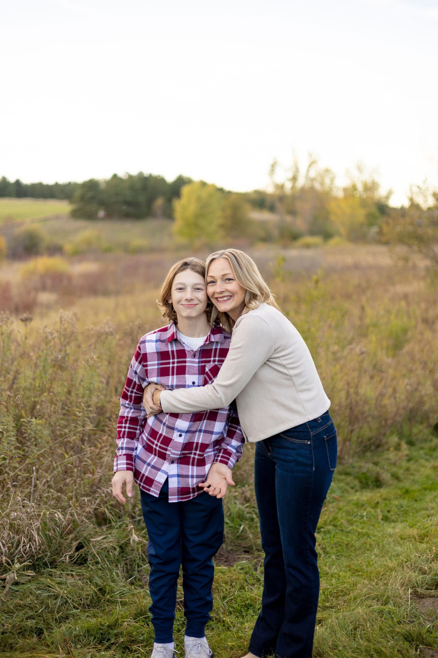 Mother hugging her teenage son outdoors in an autumn field, both smiling warmly.