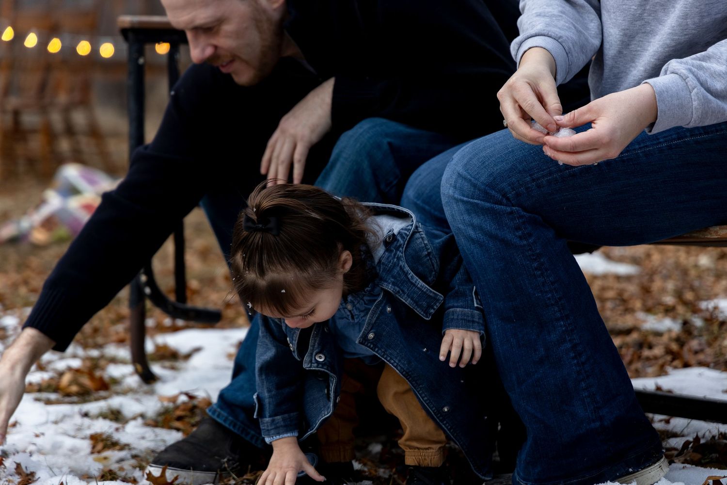 A young toddler explores snowy ground while parents watch during a winter family photo session.