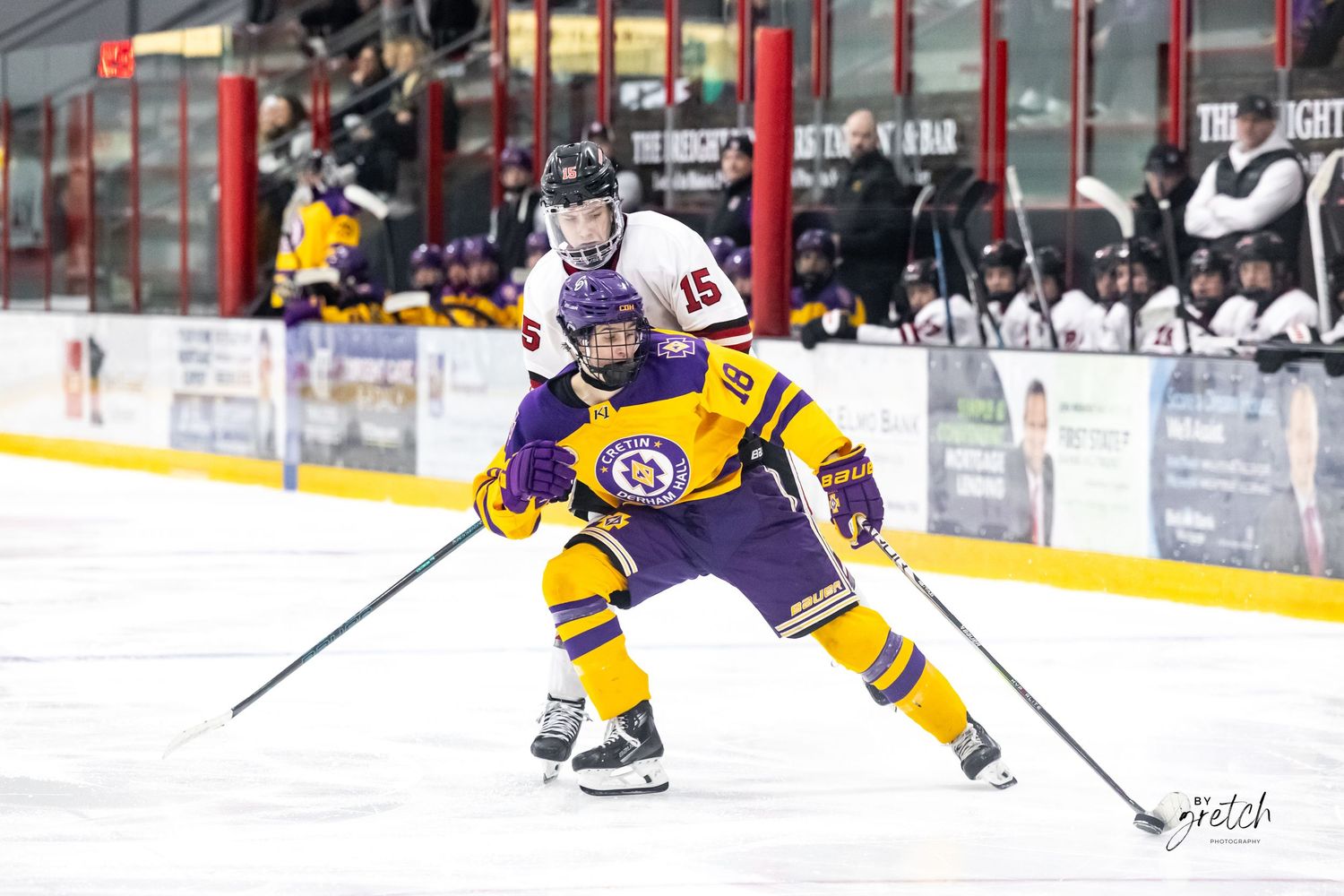 Two ice hockey players battling for puck during competitive youth hockey game.