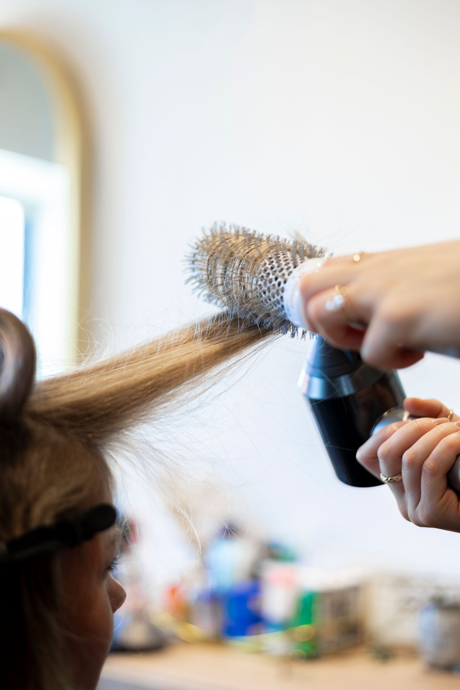 Close-up of a hairstylist blow-drying and round-brushing a client's blonde hair.