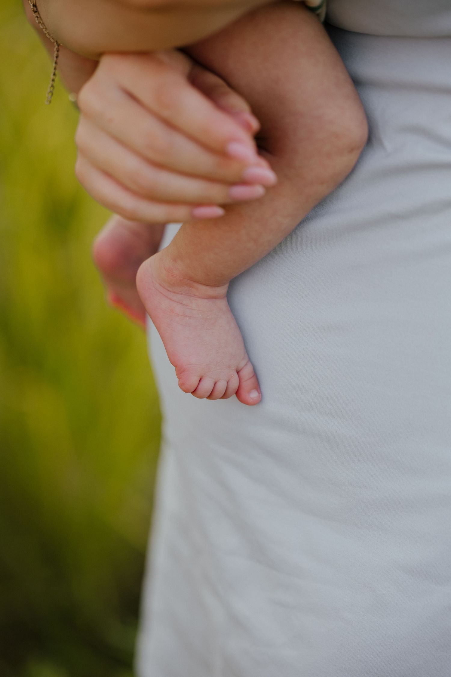 Close-up of newborn baby's tiny foot peeking out from parent's arms against white fabric.
