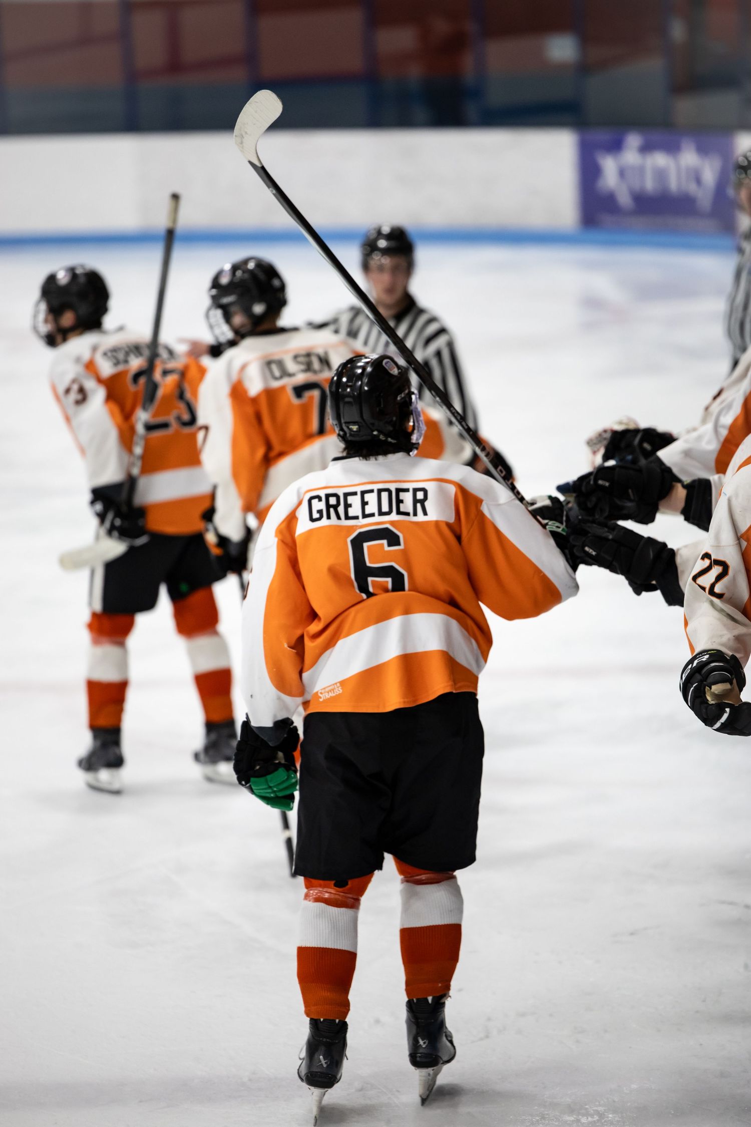 Hockey player Greeder number 6 in orange jersey celebrating with teammates on ice rink.