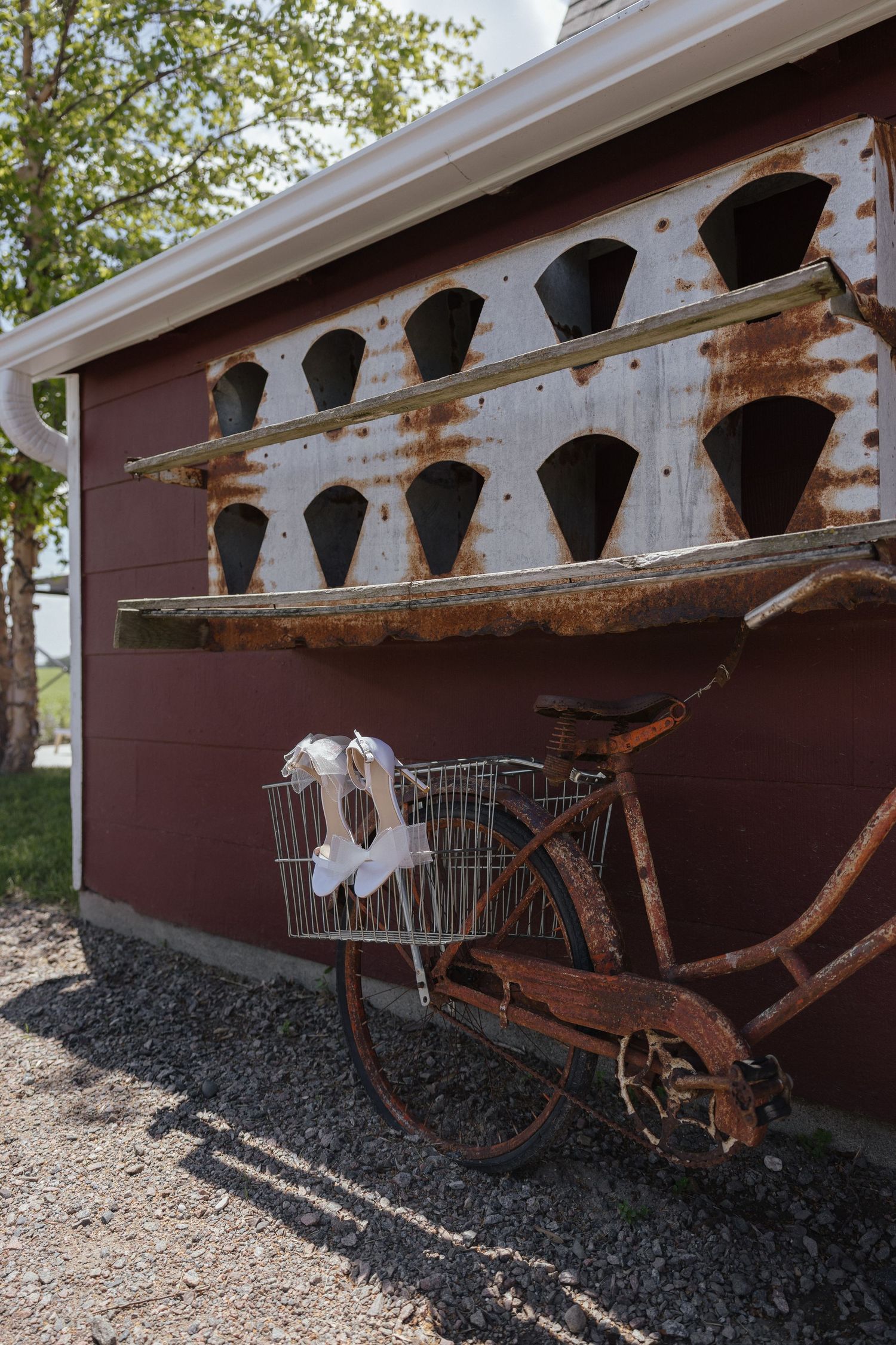 Rustic vintage bicycle with wire basket holding white fabric leaning against a red barn wall outdoors.
