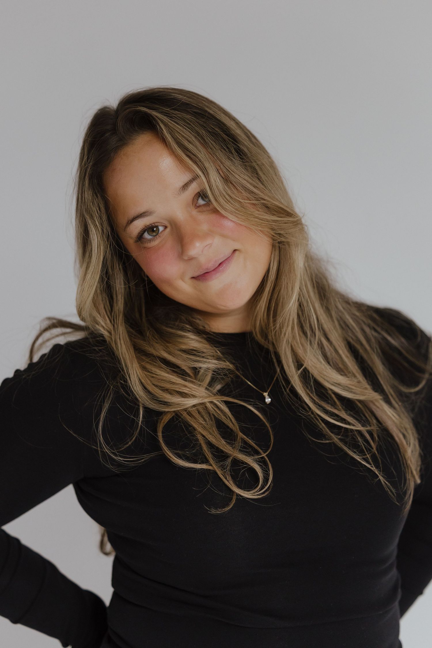 Woman with long blonde hair in black turtleneck smiling warmly at camera.