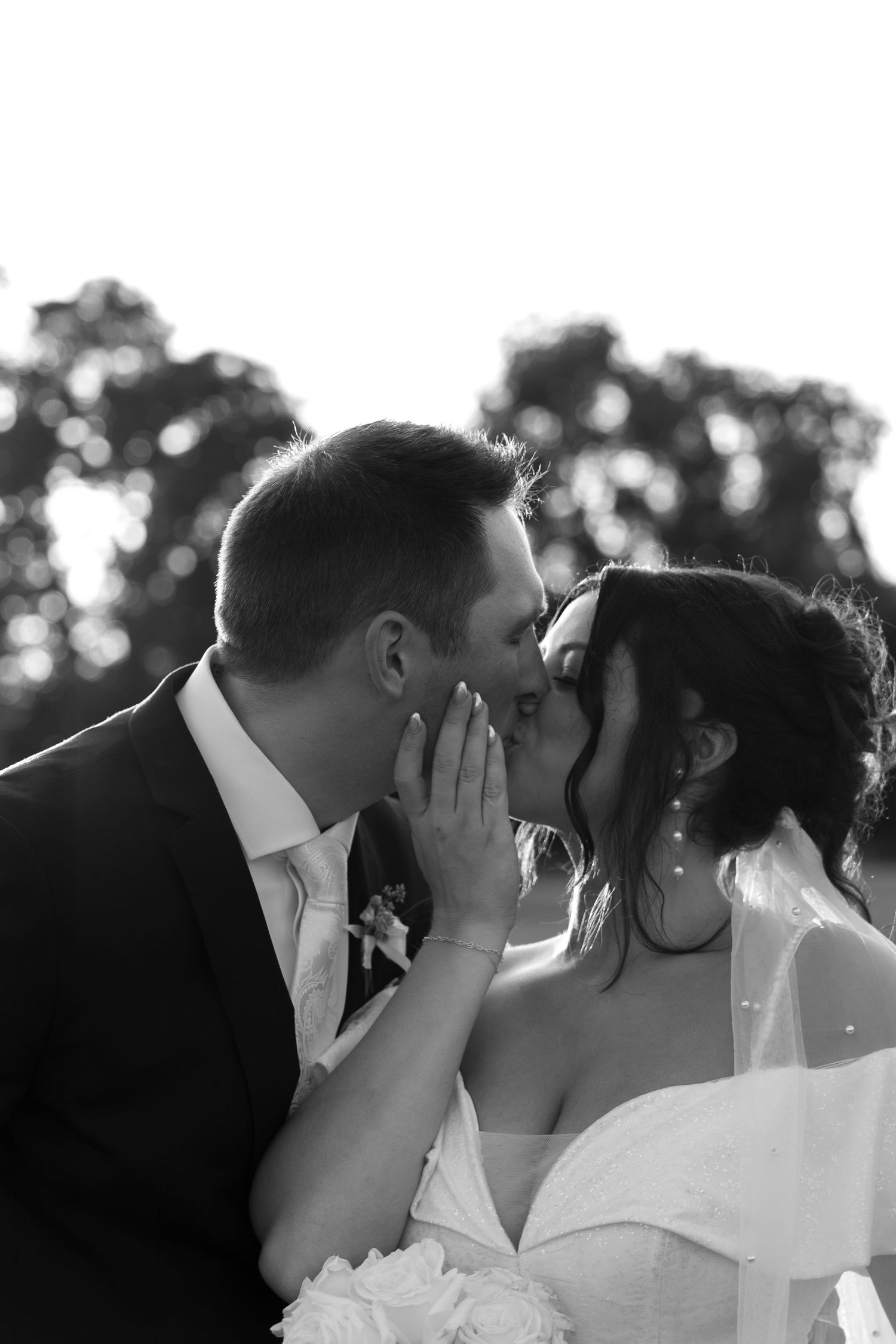 Black and white close-up of bride and groom sharing a romantic kiss outdoors.