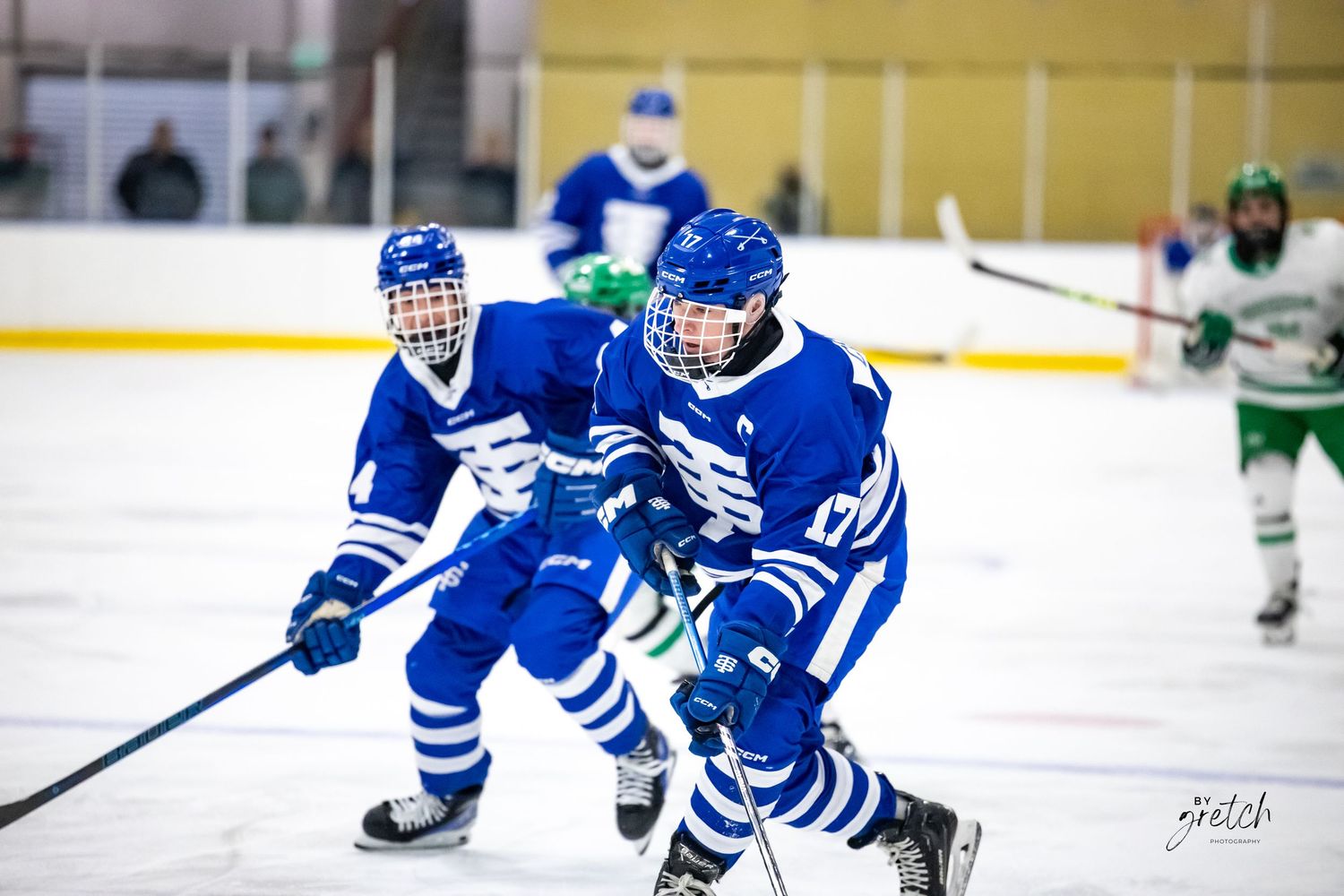 Blue and white youth hockey players skating with puck during competitive ice hockey game.