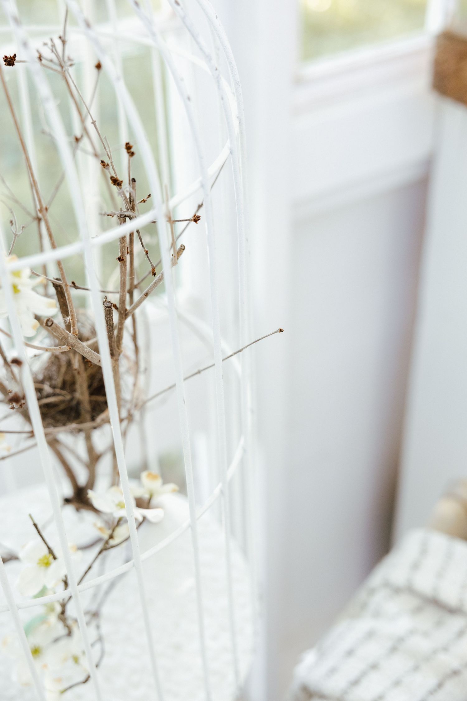 White decorative wire arch with bare branches and a bird nest, styled as elegant indoor botanical decor.