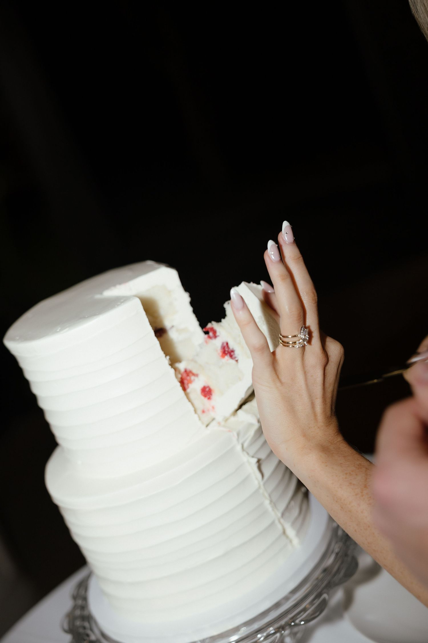 Close-up of bride cutting white ribbed wedding cake revealing red velvet interior filling.