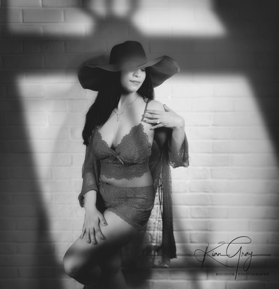 Black and white boudoir photo of woman in lace dress and wide brim hat.