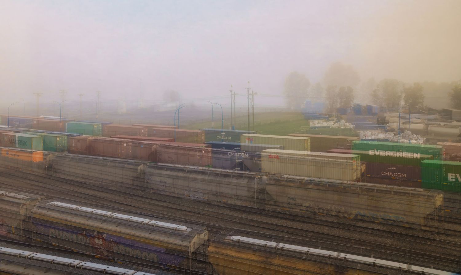 Foggy rail yard with colorful freight containers stacked on trains, including green Evergreen containers, on multiple tracks.