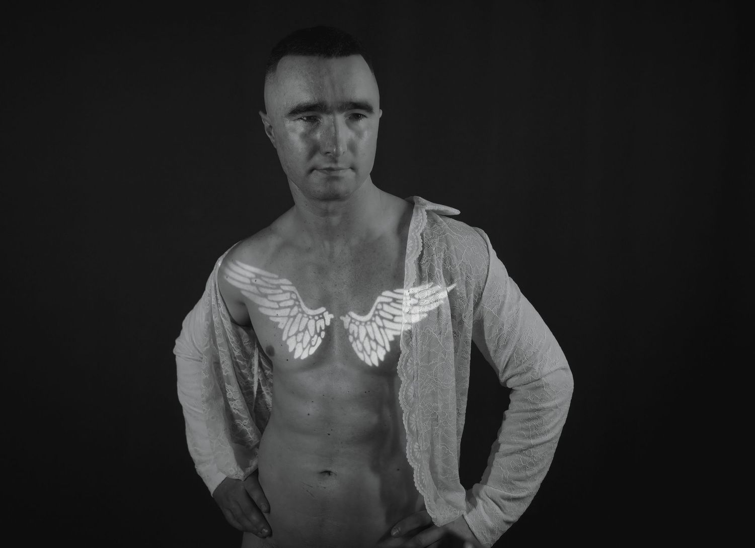 Black and white photo of man in open shirt with glowing angel wings projected on his chest.
