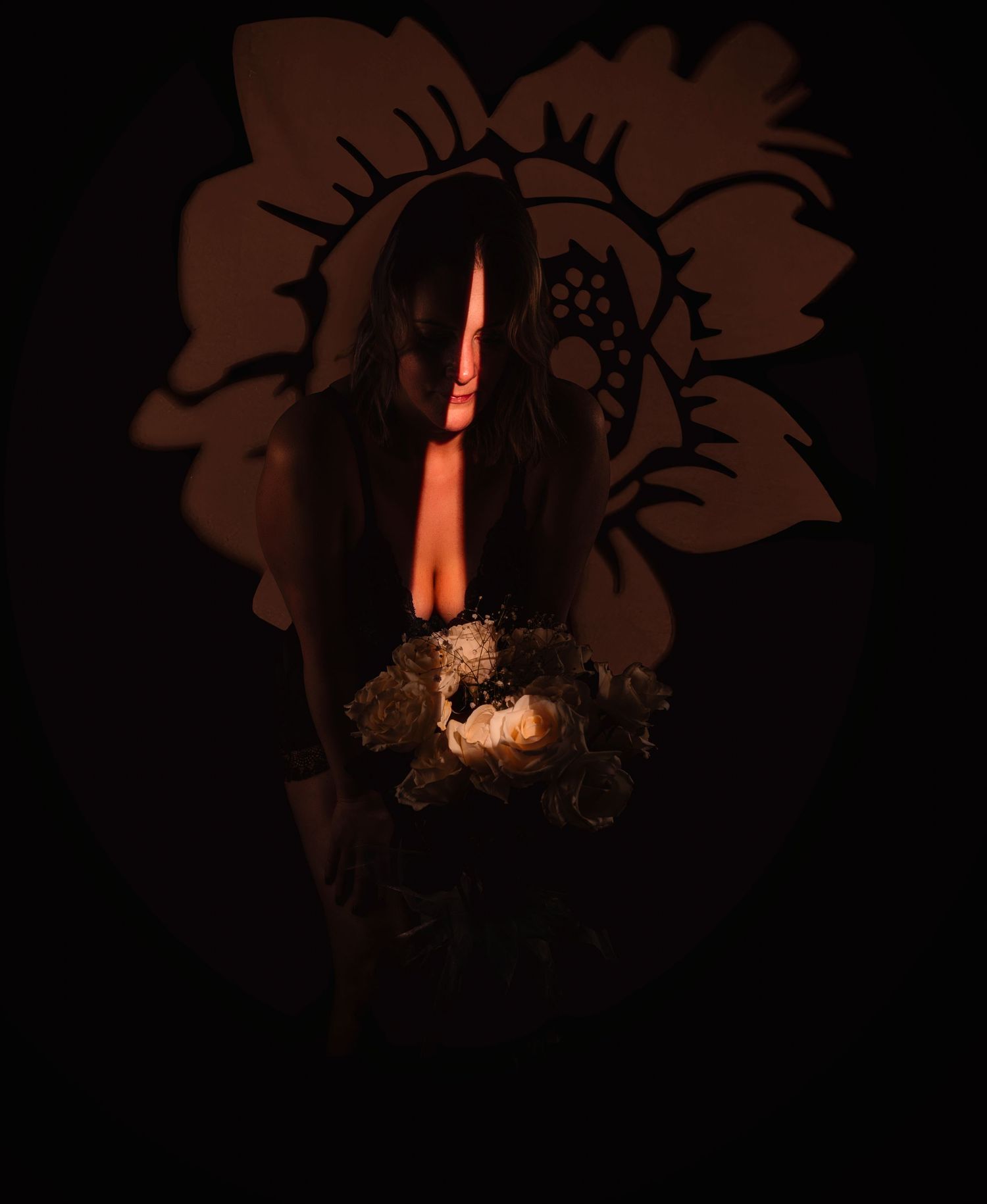 A woman holds flowers in dramatic dark lighting with a floral shadow projection behind her.