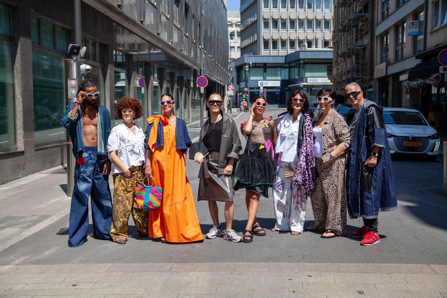 Group of stylishly dressed people posing together on a sunny urban street in a European city.