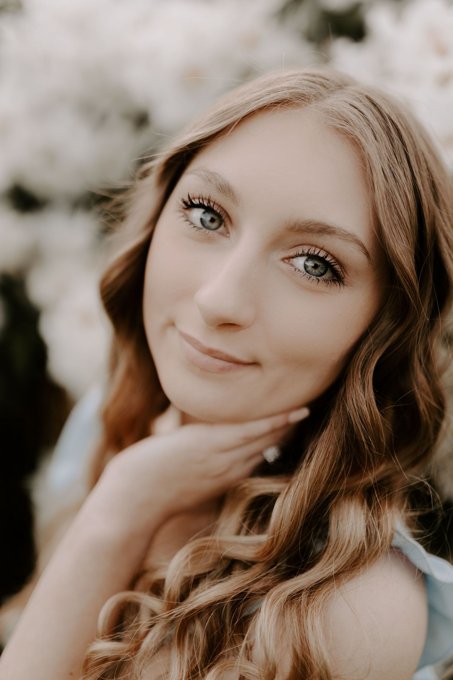 Soft portrait of young woman with wavy hair and gentle smile against blurred background.