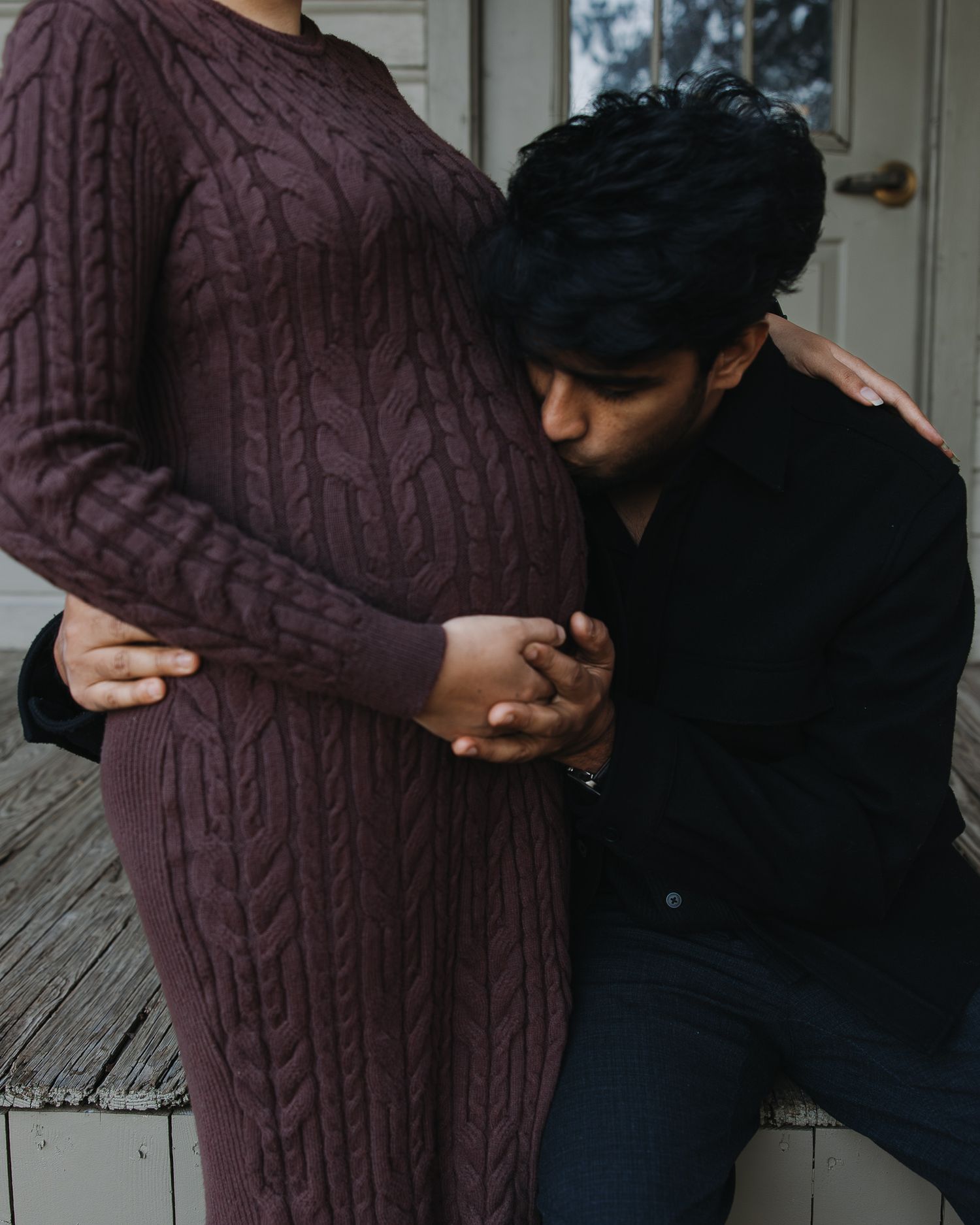 Couple in warm knit sweaters sharing intimate moments on a wooden porch.